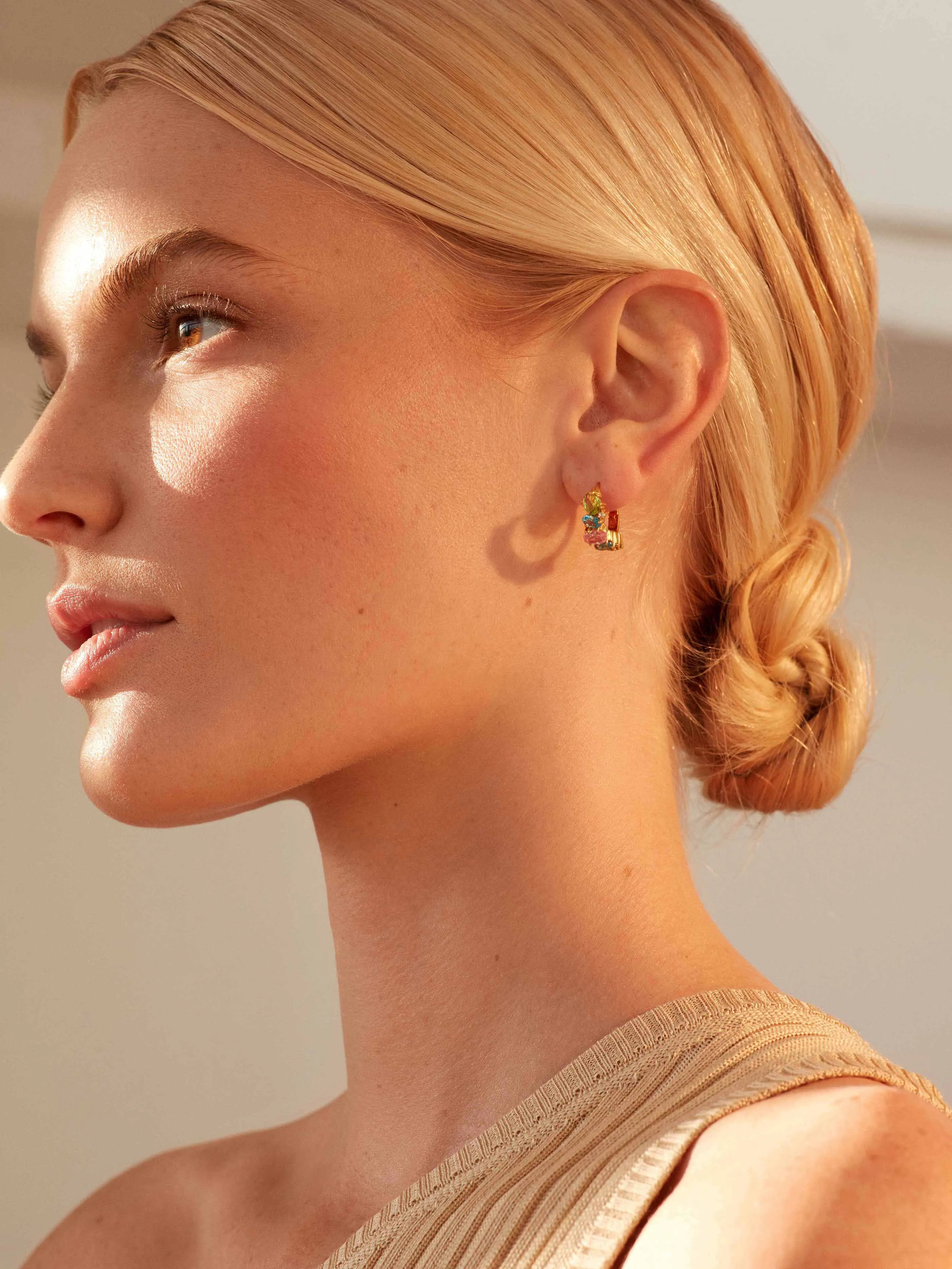 A vibrant summer woman wearing the SHYLA - Nila Huggies Multi - Gold earrings with gold hoops and vibrant colored stones.