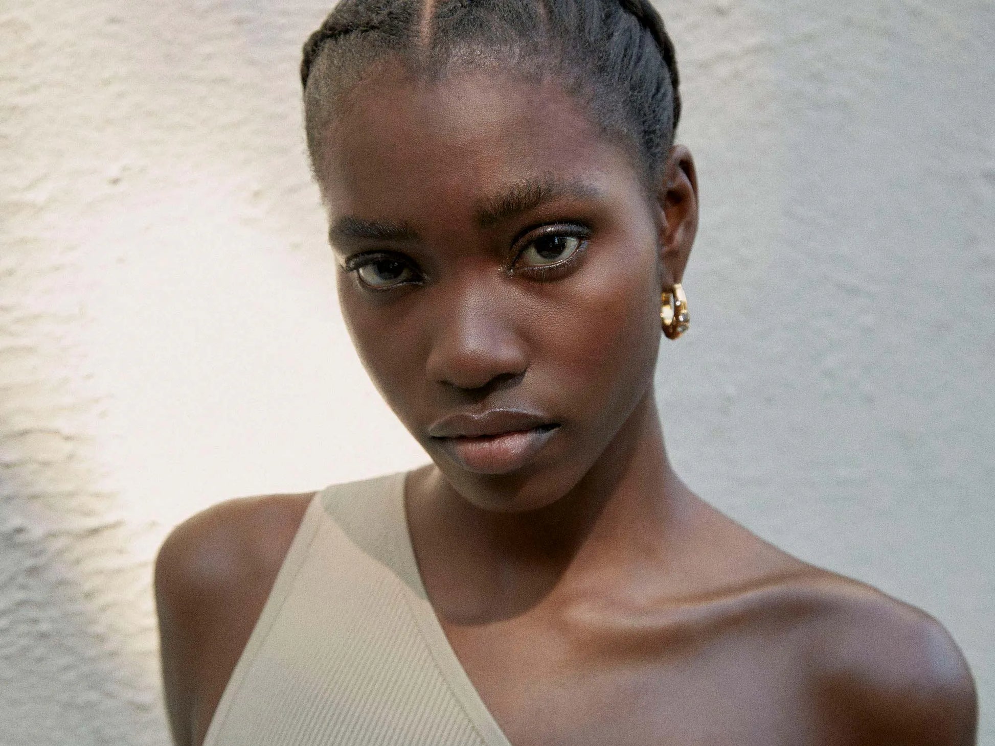 A black woman wearing a beige top and medium-sized chunky hoop earrings with crystals, known as Shyla - Oren Hoops - Gold.