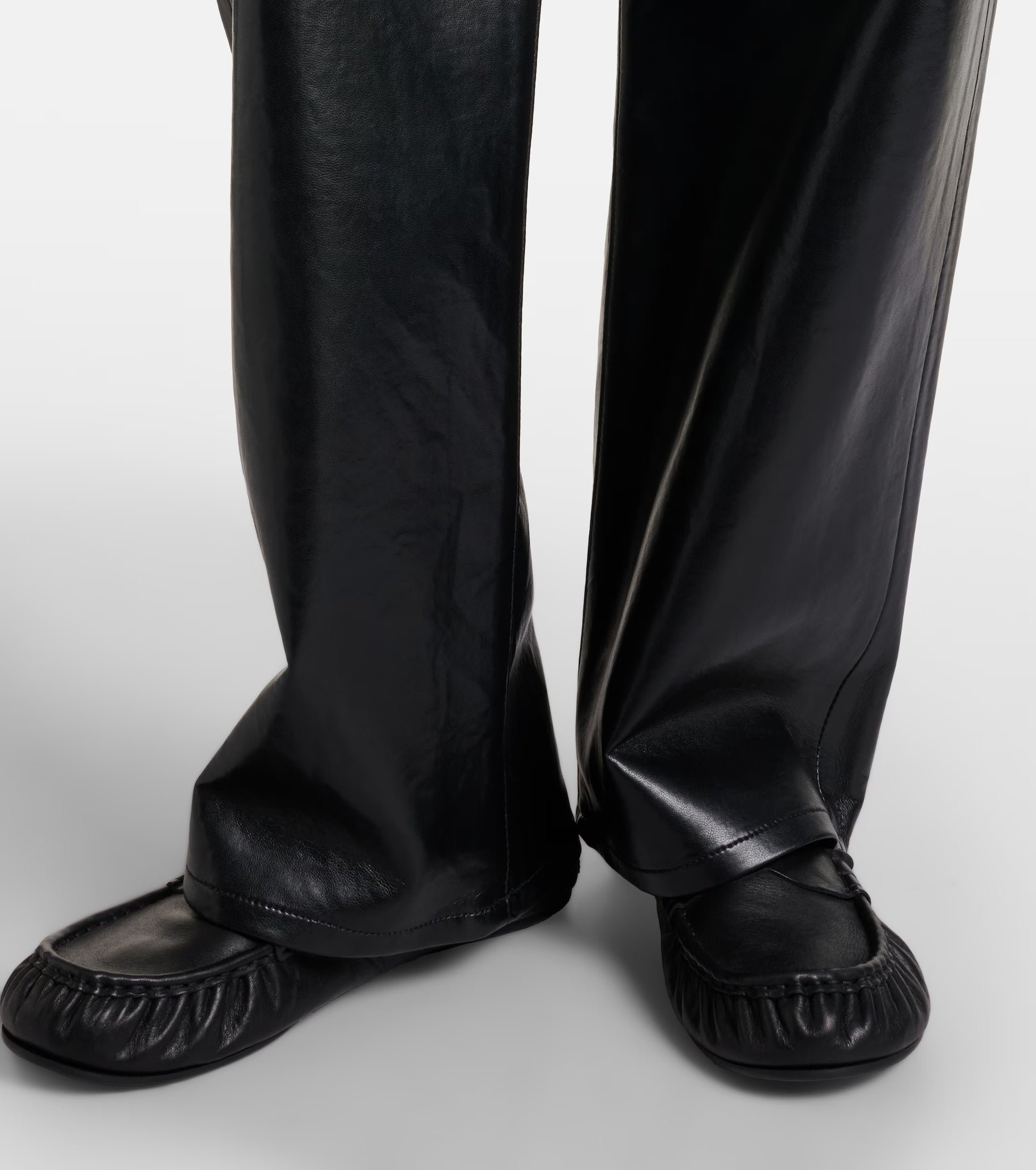 Close-up of a person wearing the AGOLDE Arc Jean 32 Wide Leg Trousers - Detox and black slip-on shoes, standing on a white background.