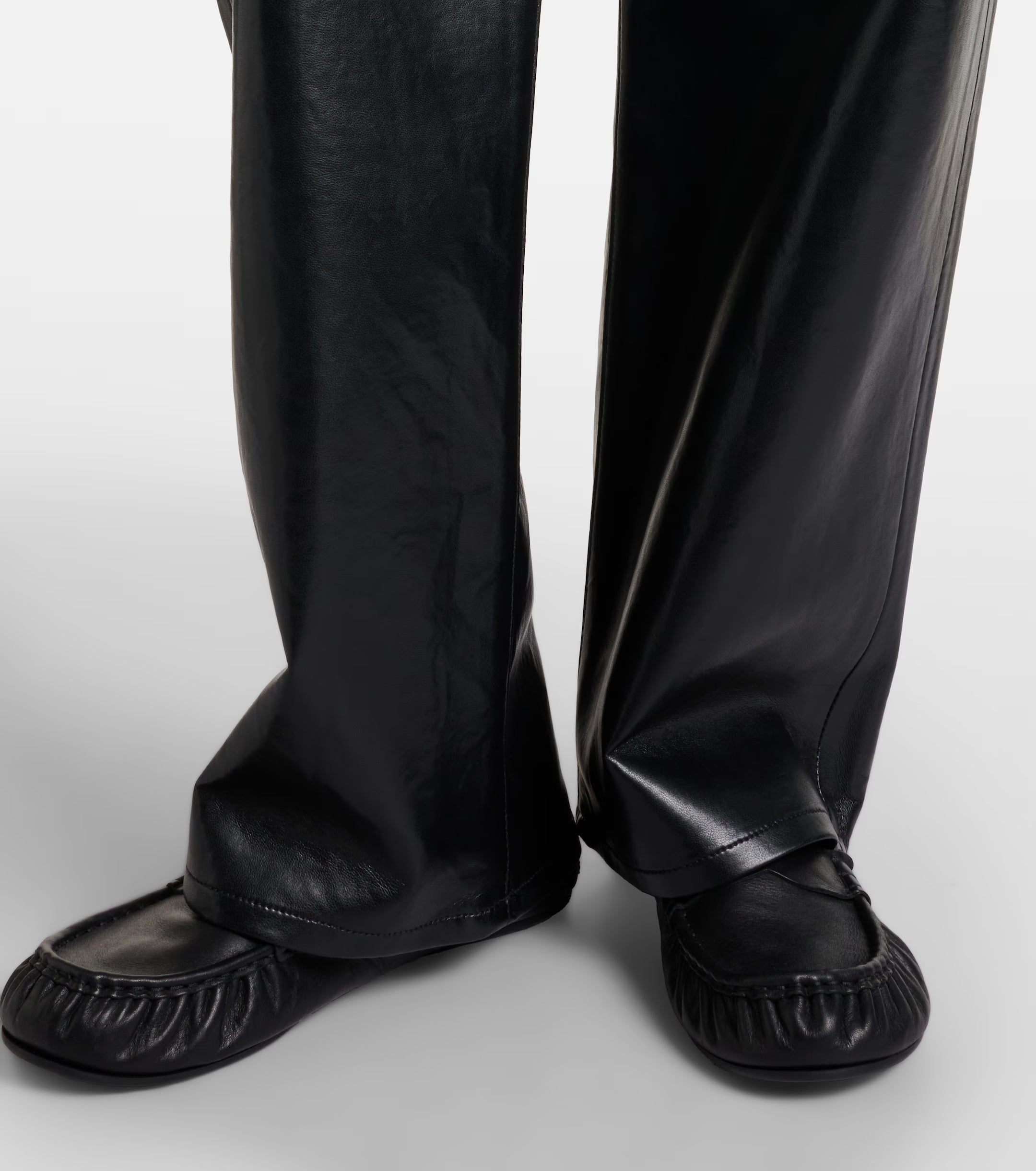 Close-up of a person wearing the AGOLDE Arc Jean 32 Wide Leg Trousers - Detox and black slip-on shoes, standing on a white background.