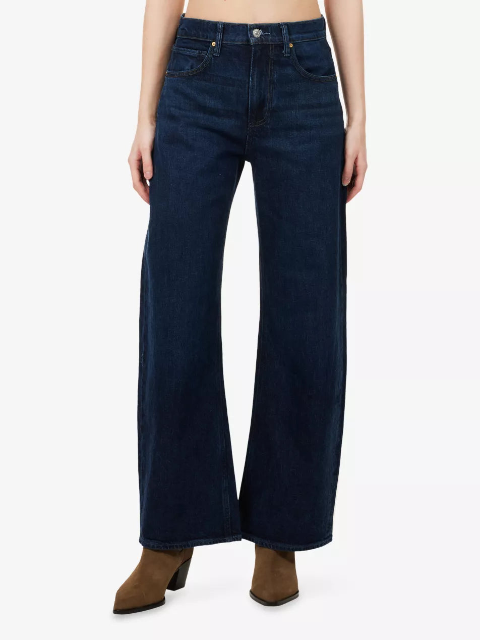 A person wearing Paige Arellia Skimmer Barrel Leg - Visage jeans, a high-rise barrel leg style in a dark vintage-inspired wash with front pockets, paired with brown heeled boots, shown from the waist down.