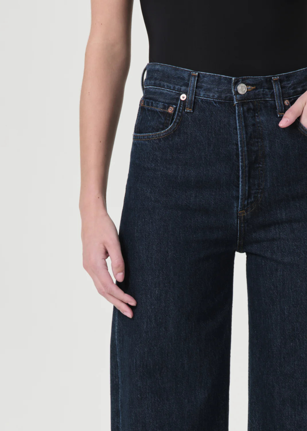 A person wearing Ren High Rise Wide Leg Jeans - Polished by AGOLDE and a black top, with their right hand in the front pocket.