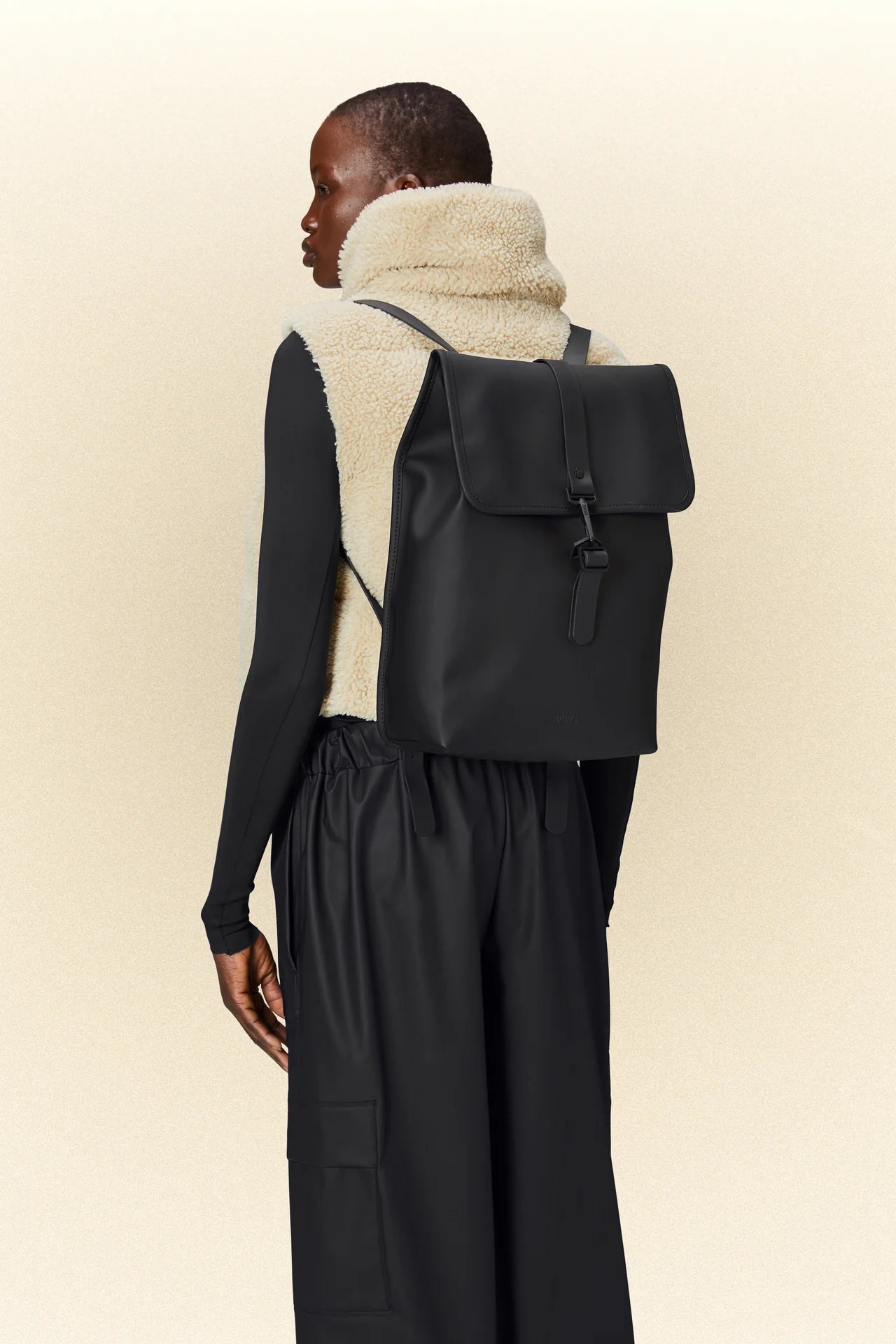 A woman wearing a black Rains waterproof backpack.