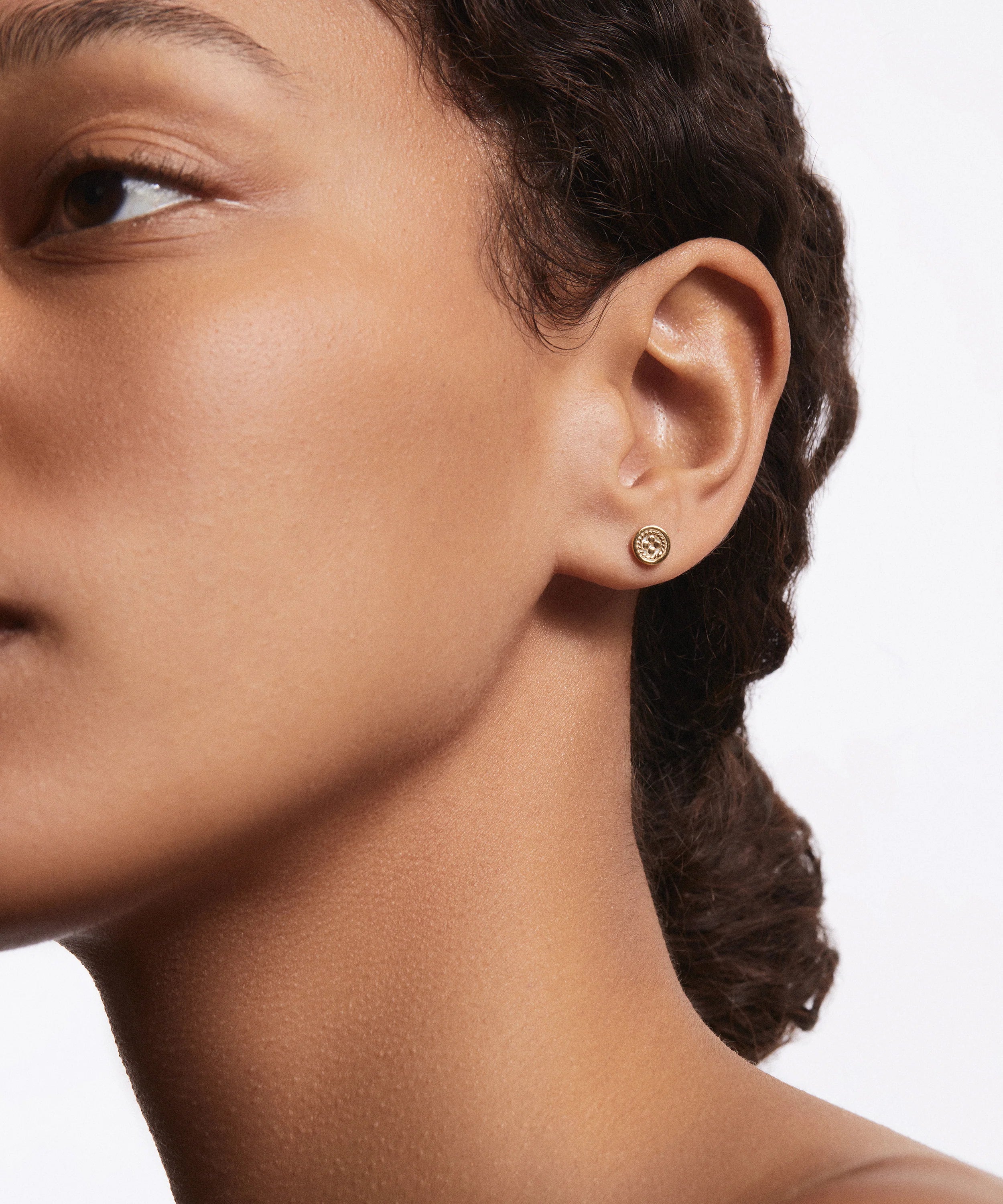 Close-up of a woman's face in profile, wearing Anna Beck's Circle Stud Earrings in 18k gold, set against a plain white background.