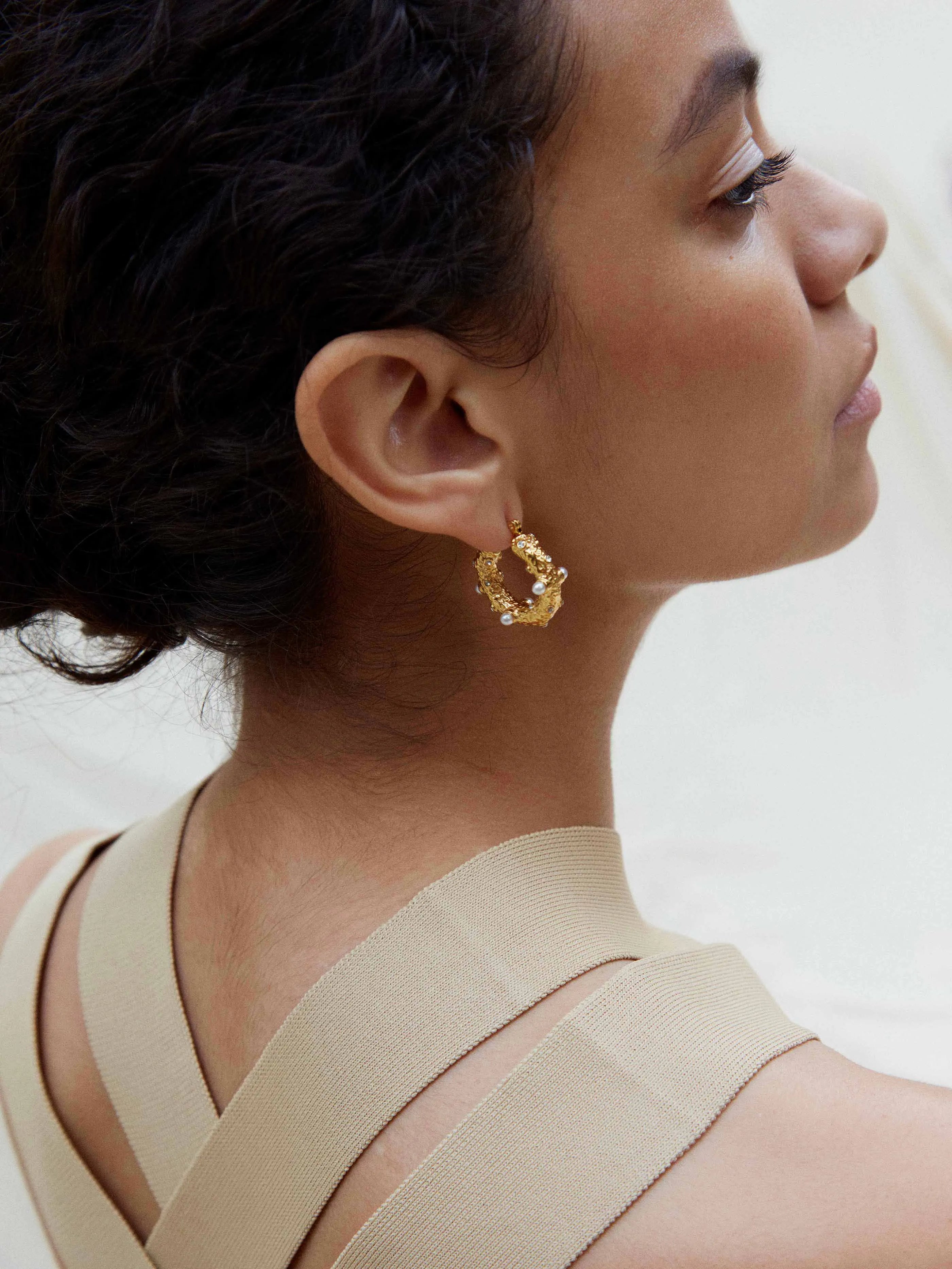A woman wearing a tan top and SHYLA - Sirius Hoops- Gold earrings.