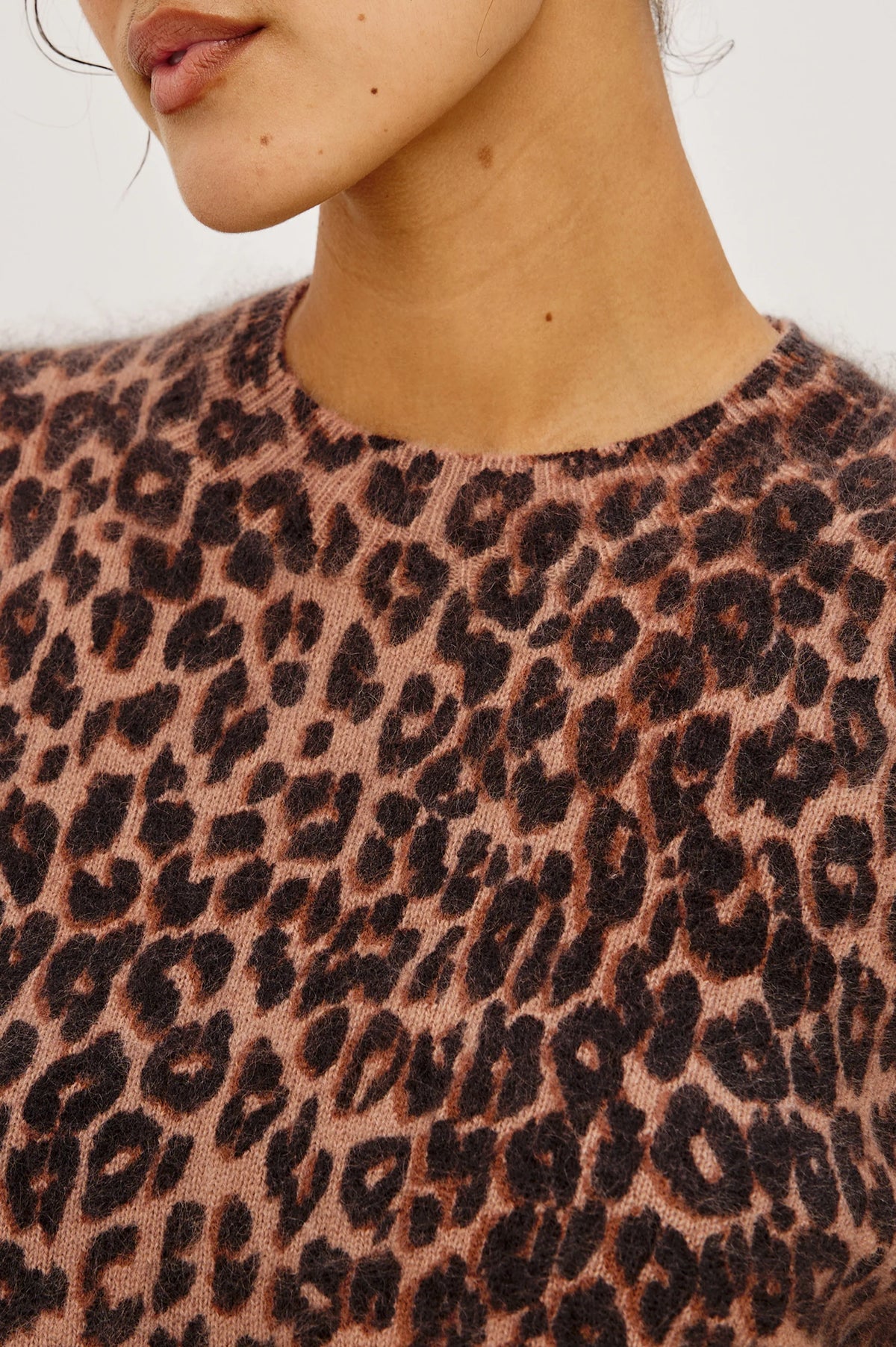 Close-up of a person wearing the Sofia Sweater - Brown Nala by Rails, featuring a brown and black leopard print cashmere design, showing part of the face, neck, and upper torso.