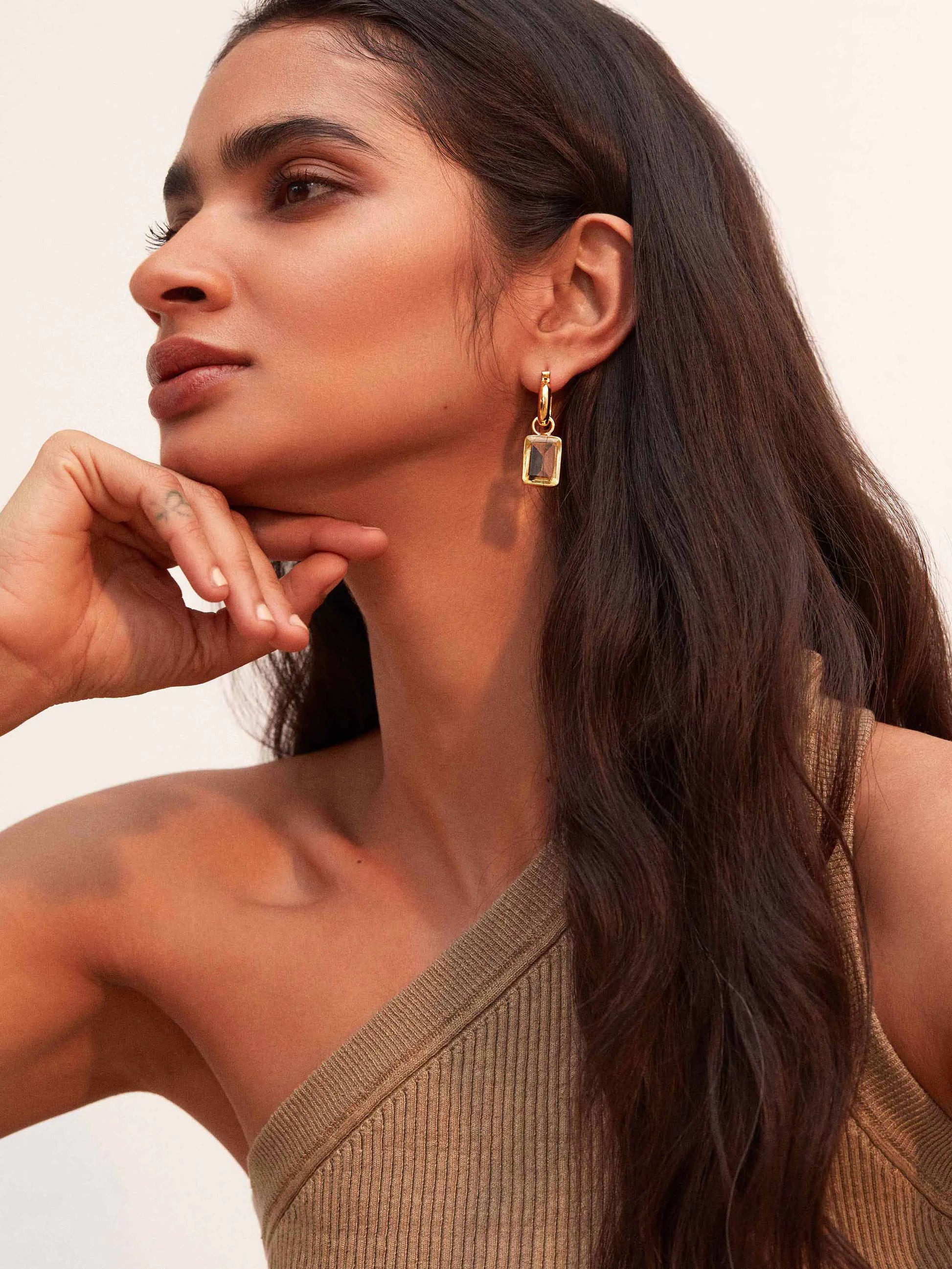 A woman wearing a tan top and SHYLA - Sorrento Hoops- Gold earrings by Shyla.