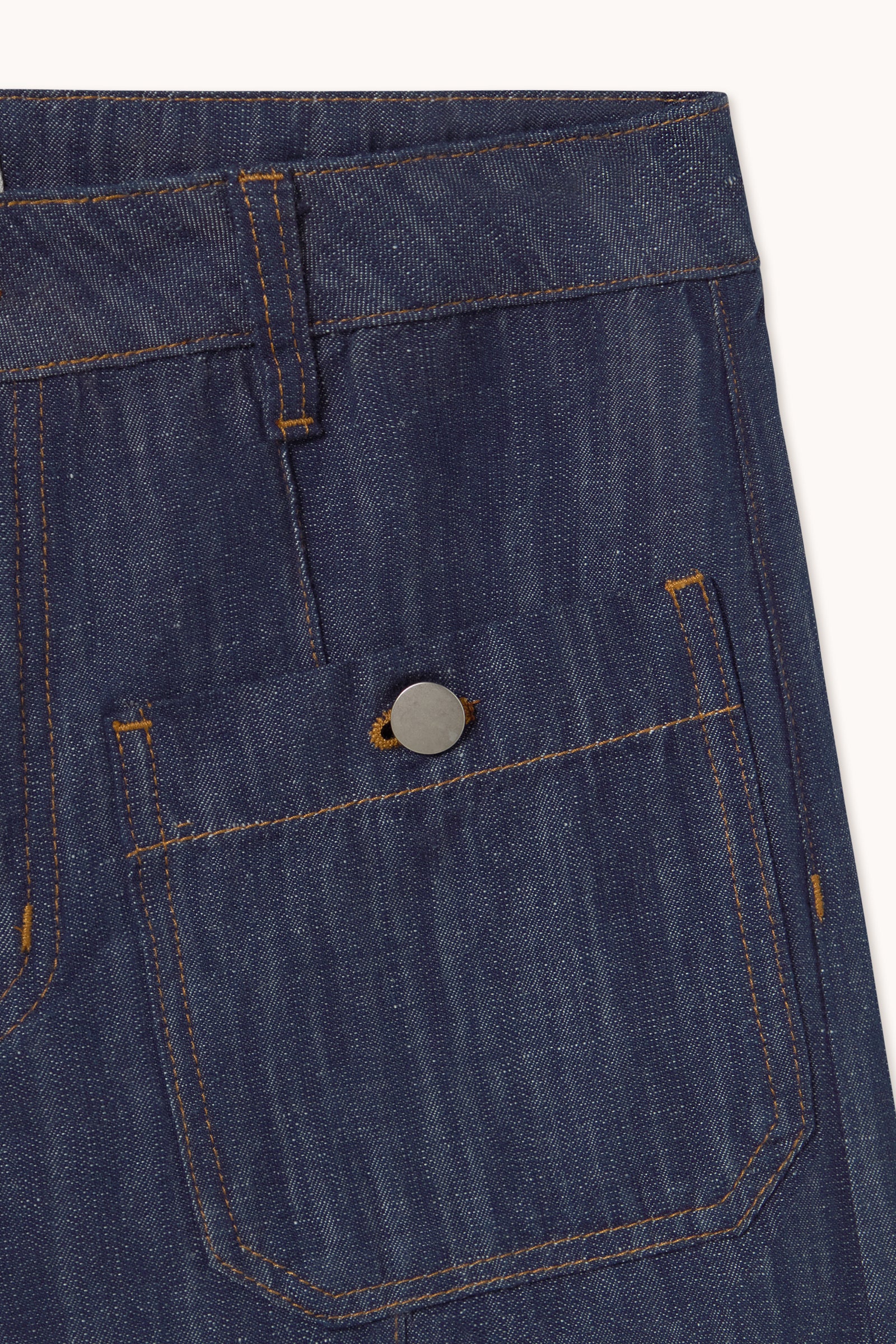 Close-up of indigo blue denim fabric with orange stitching and a metal button on the pocket flap—signature details of Tiny Big Sister’s Wide Leg Linen/Denim Trousers.