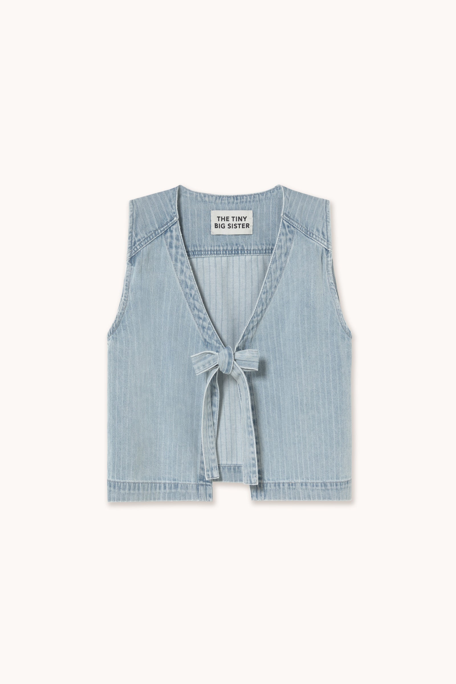 The Tiny Big Sister Denim Tie-Vest in Light Blue features a pinstripe, sleeveless design with a chic tie-front closure, shown on a plain background.