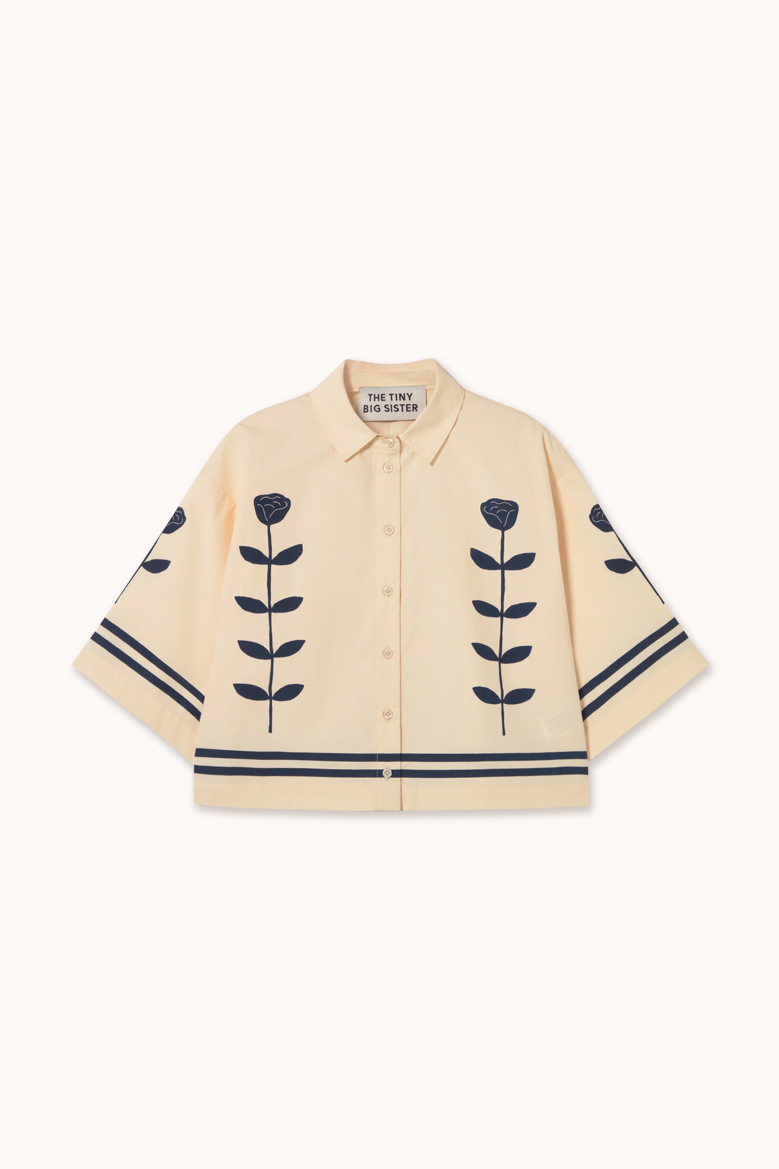 The Flower Shirt - Ivory by Tiny Big Sister is a cream-colored, oversized boxy shirt with dark blue floral motifs and striped patterns on the front and sleeves.