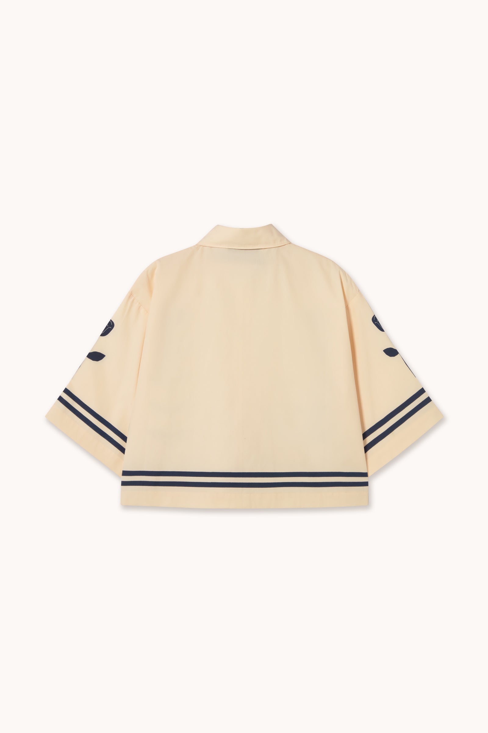 Back view of the Flower Shirt - Ivory by Tiny Big Sister: cream shade, oversized boxy fit, short sleeves, collar, navy blue stripes on sleeves and hem, plus navy leaf-shaped accents on upper sleeves.