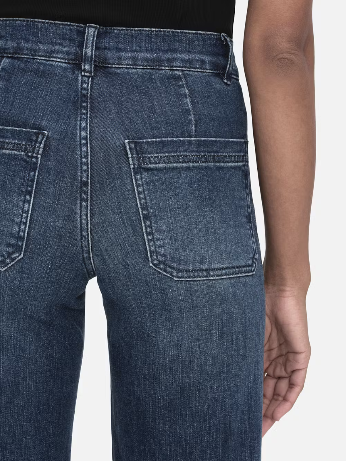 Model wears wide leg jeans in a dark wash. Features front pockets. Close up back view.