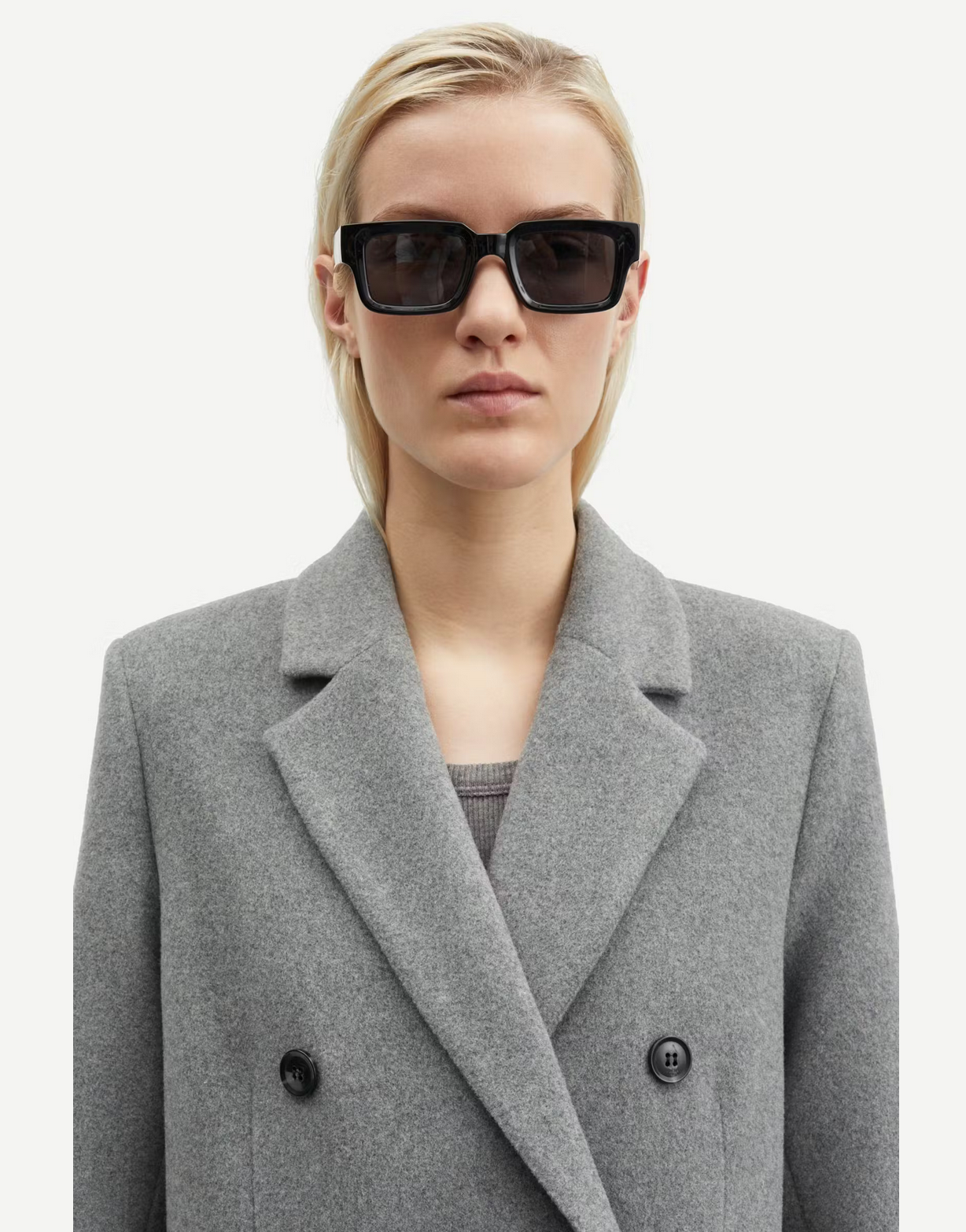 A person with short blonde hair wearing black sunglasses and an elegant Falcon Coat - Grey Melange by Samsøe Samsøe.