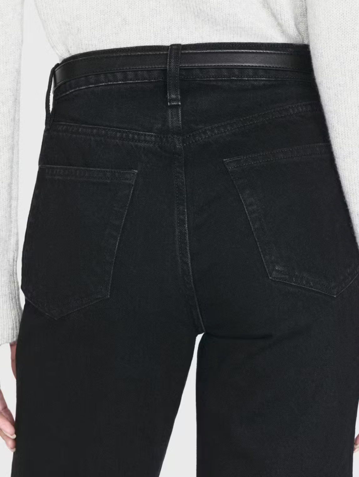 Rear view of a person wearing Frame's Le Jane Crop Raw Fray black denim jeans with back pockets and a black belt. The high-rise jeans are complemented by a light gray sweater, creating a timeless look.