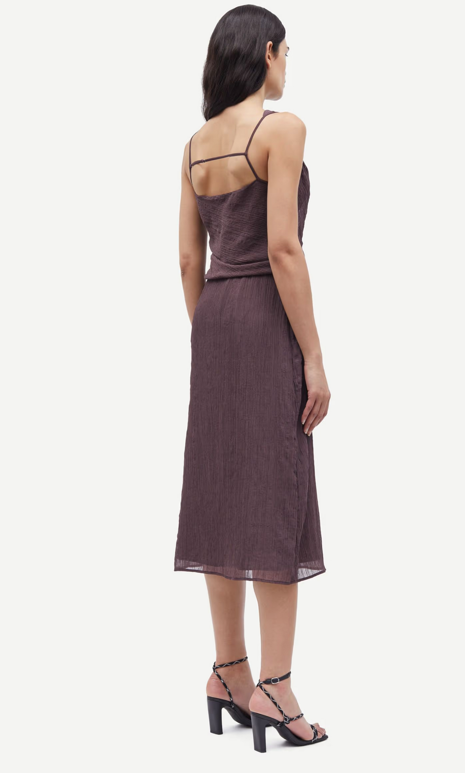 A woman in Samsøe Samsøe's Savira Top - Raisin, a sleeveless ruched recycled polyester piece with thin straps, stands elegantly in three-quarter view paired with black heeled sandals.