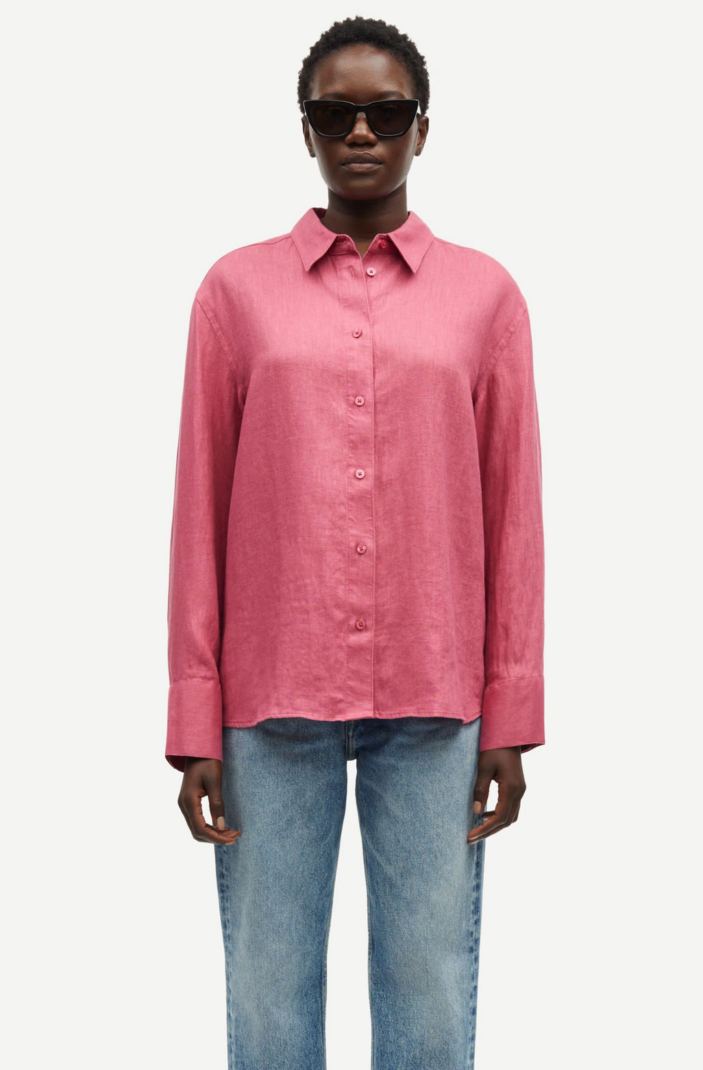 A person wearing sunglasses, the relaxed fit Sanot Shirt - Rose by Samsøe Samsøe, and blue jeans stands against a white background.