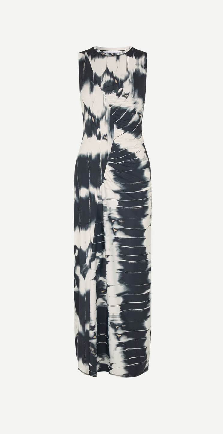 The Saandreas Dress by Samsøe Samsøe is a black and white tie-dye jersey maxi dress featuring a fitted waist, long skirt, and is sustainably crafted from recycled polyamide.