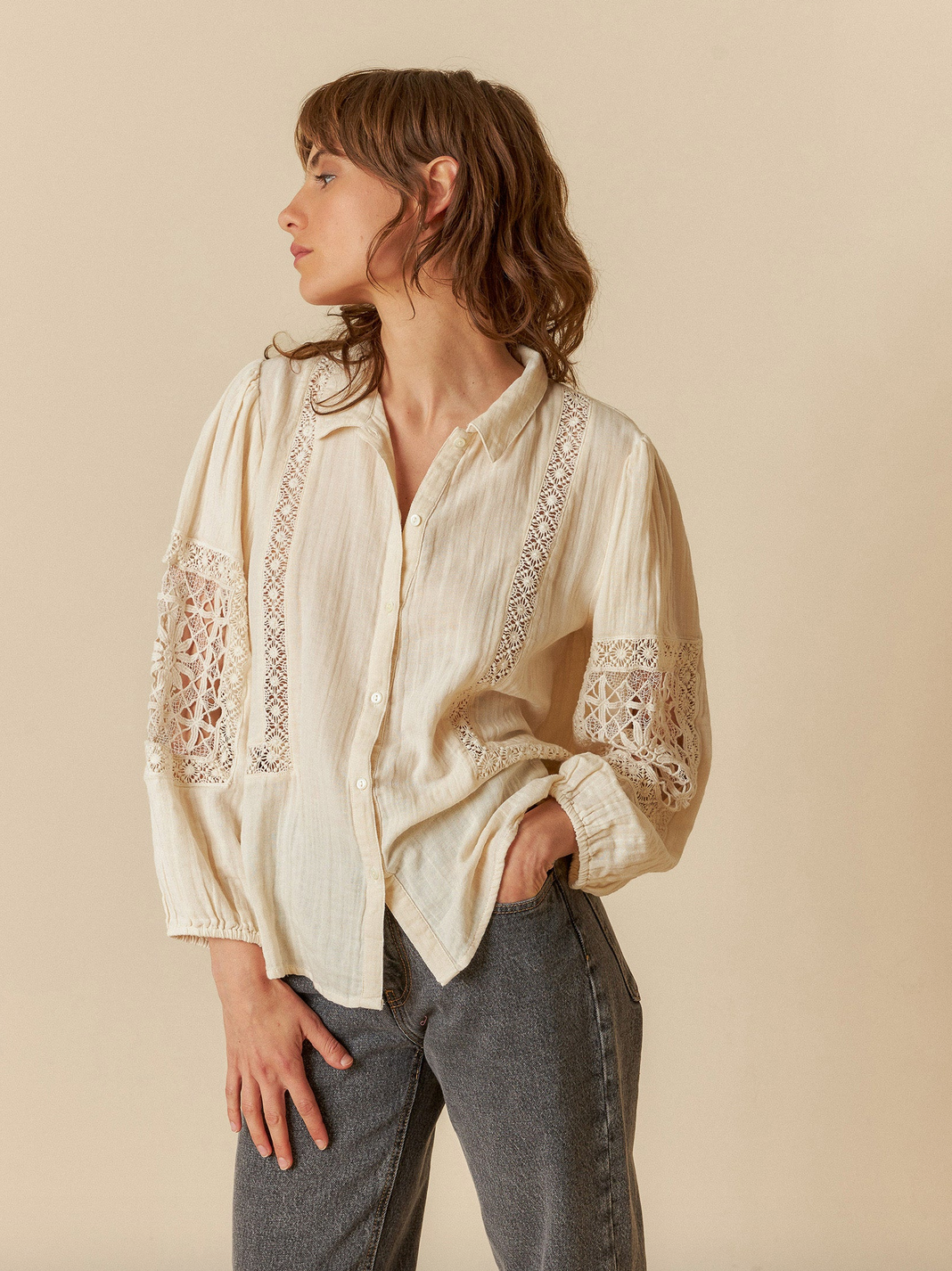 A person in an ivory Double Gauze Shirt from Indi & Cold and gray pants stands against a beige backdrop, looking sideways. The relaxed fit enhances the ensemble's effortless charm.