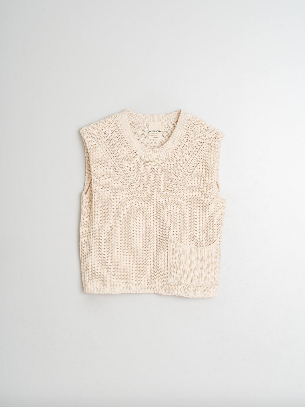 The English Rib Knit Vest - Ivory by Indi & Cold is a beige, sleeveless, organic cotton knit with a round neck and right-side pocket. Photographed on a white background, it's a versatile wardrobe staple.