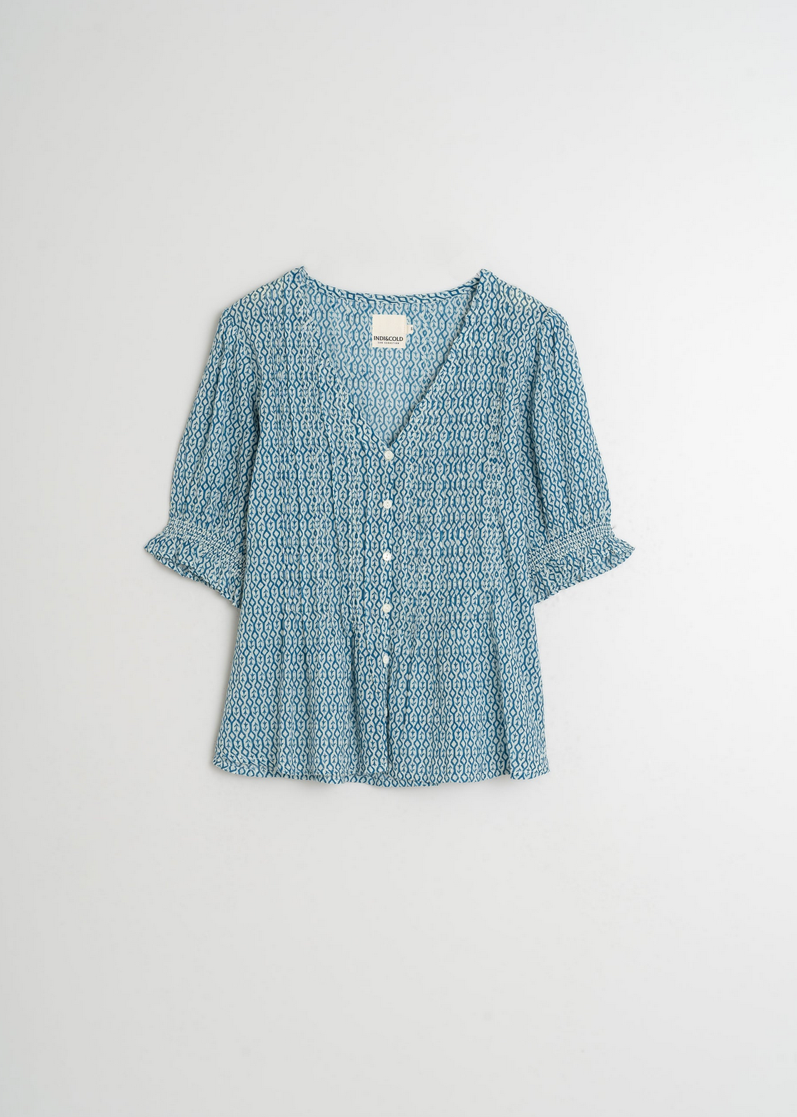 The Indi & Cold Short Sleeve Blouse in blue features a geometric print, V-neckline, button front, and flared sleeves against a plain backdrop.