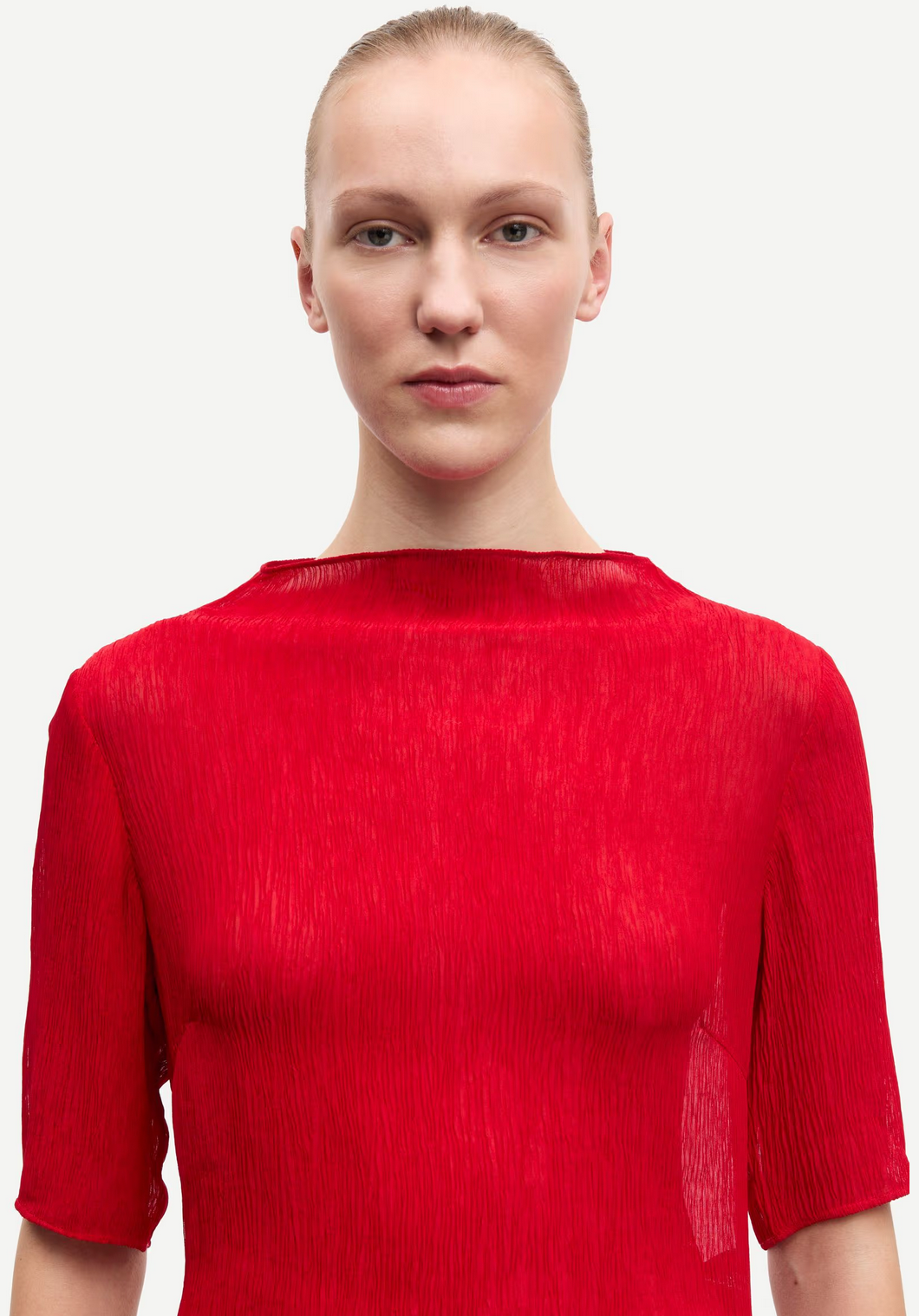 A person with slicked-back hair wears the Samsøe Samsøe Samiller Top in Haute Red, a short-sleeved semi-sheer top made from recycled viscose, standing against a plain white background.