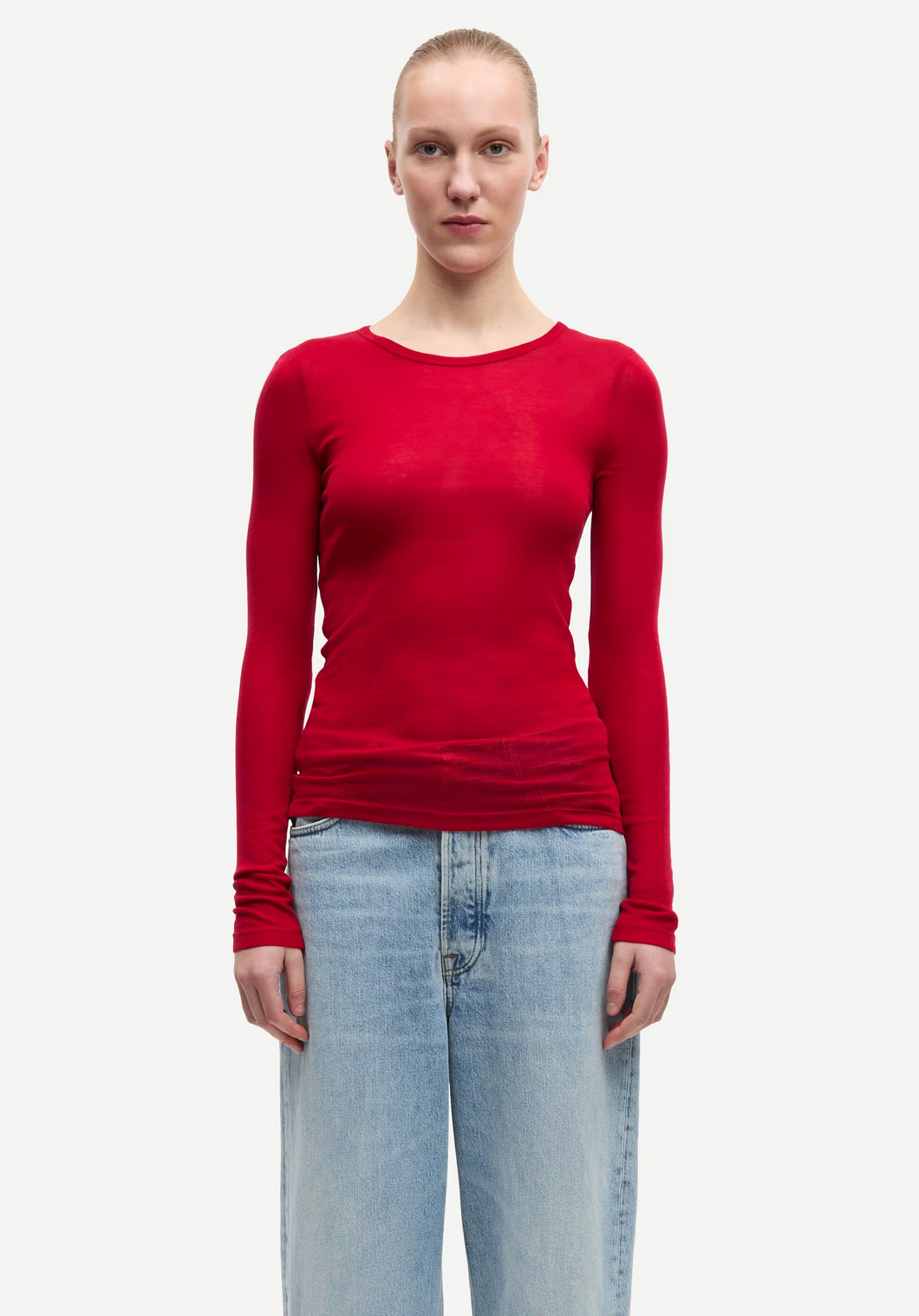 A person wears the Samsøe Samsøe Sadou T-shirt Long Sleeve in Haute Red with light blue jeans, standing facing forward against a plain white background.