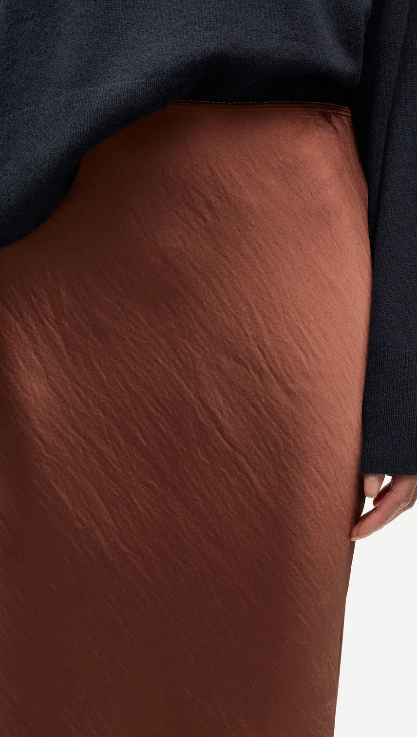 A person wearing a dark sweater and the Samsøe Samsøe Saagneta Long Satin Skirt in Tortoise Shell, with one hand resting by their side.