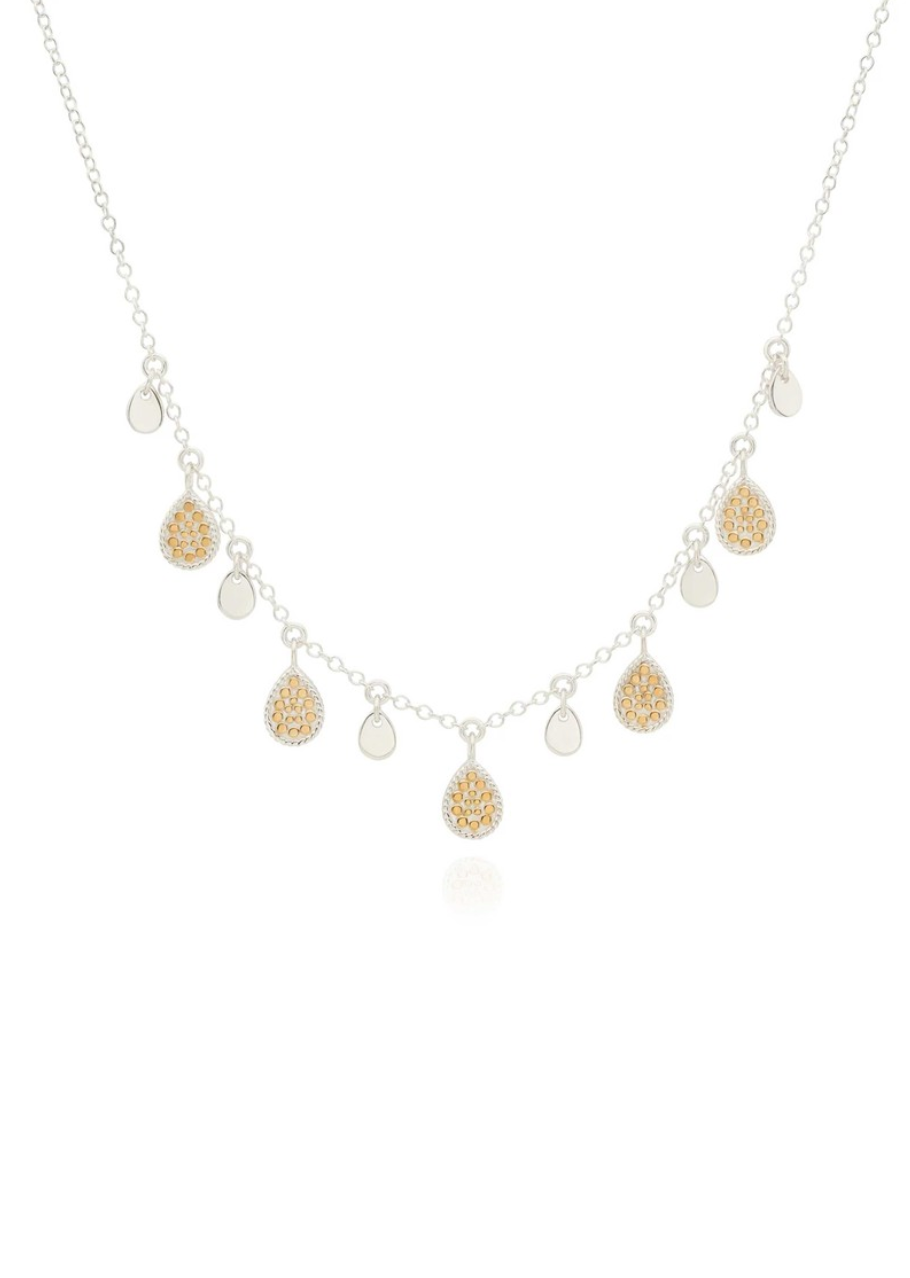 The Anna Beck Teardrop Charm Necklace is a delicate sterling silver piece with alternating round and teardrop-shaped pendants, accented by gold textured detailing.
