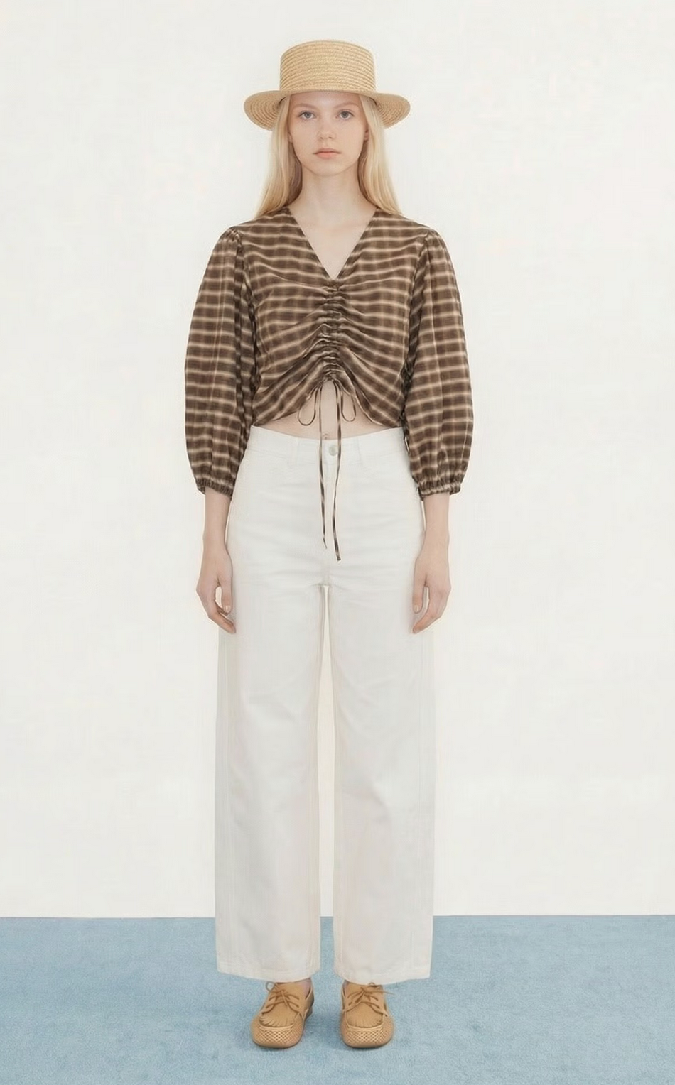 A person faces forward wearing the Tiny Big Sister Check V-Neck Blouse in brown, paired with a straw hat, white wide-leg pants, and tan shoes against a plain background.