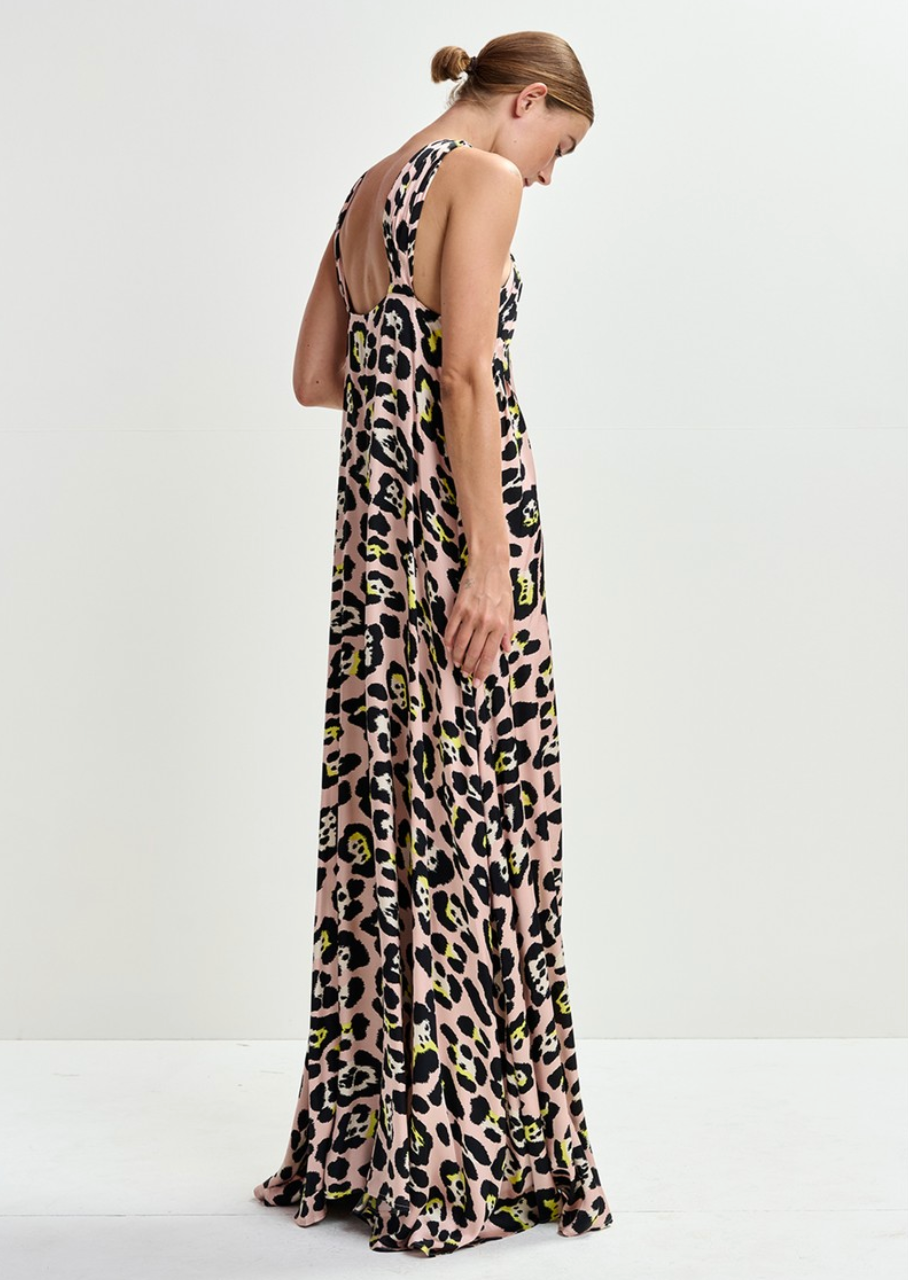 A woman models the Essentiel Antwerp Jaycee Halterneck Maxi Dress in Pink Pastel/Leopard, featuring an A-line, sleeveless, floor-length design, as she stands sideways against a plain white background.