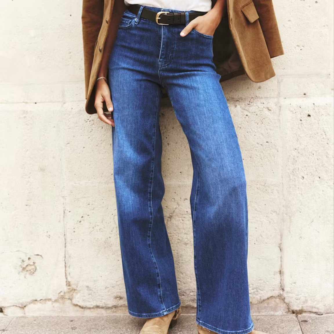 woman wearing blue jeans with a black belt, white tshirt and boots against a wall