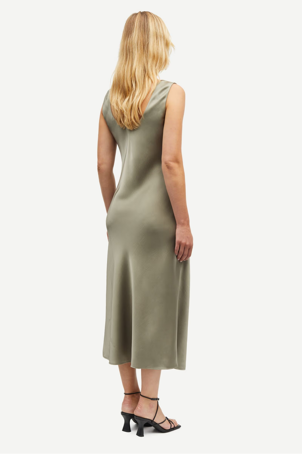 model with blond hair wears the sasumma satin midi slip dress by samsoe samsoe with black strappy sandals back view