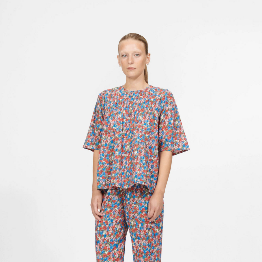 a woman wears a floral printed blouse by nue notes on a white background