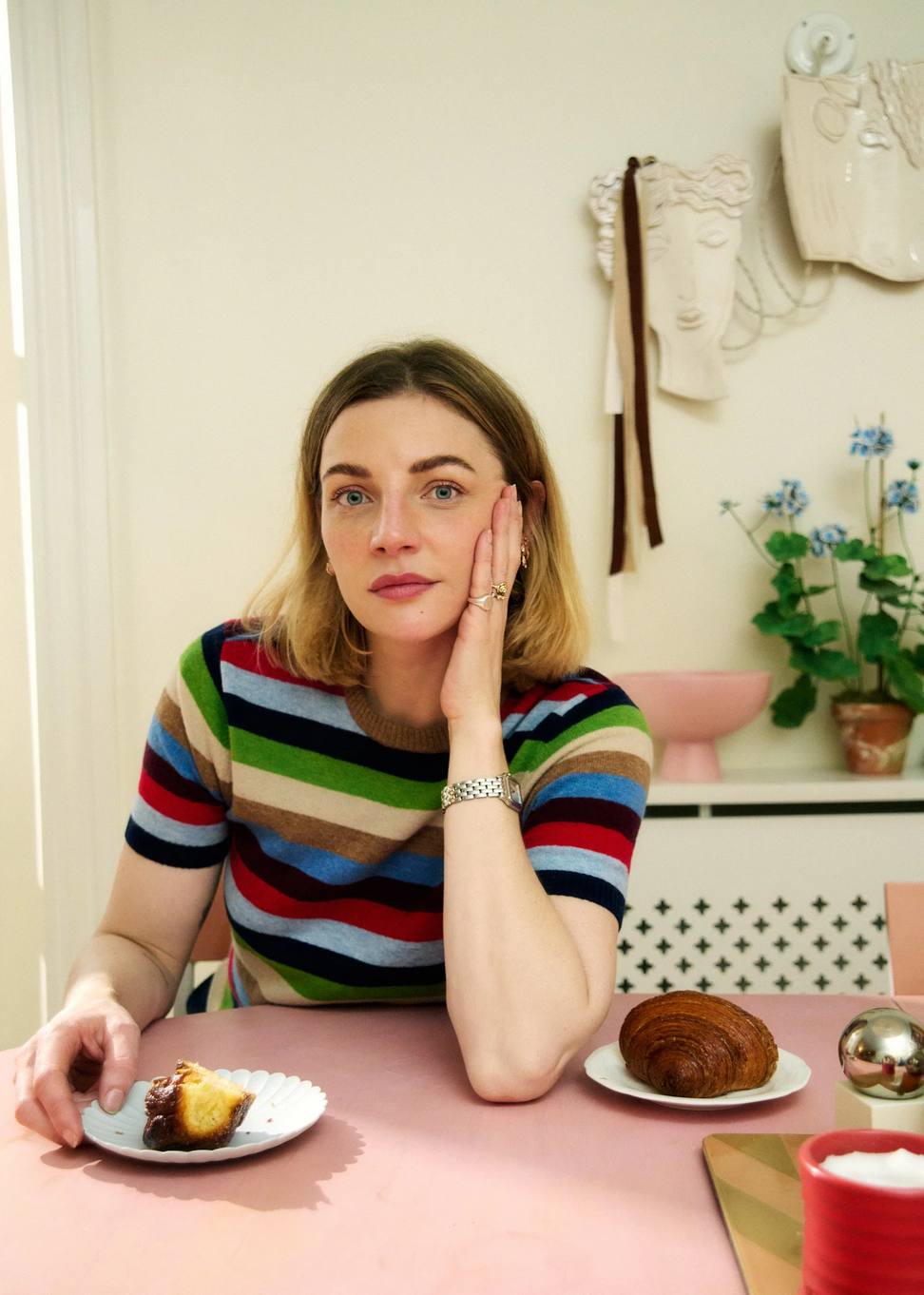 a woman wears a red, blue, green and neutral stripe wool t-shirt by nue notes while sitting at a table in a kitchen