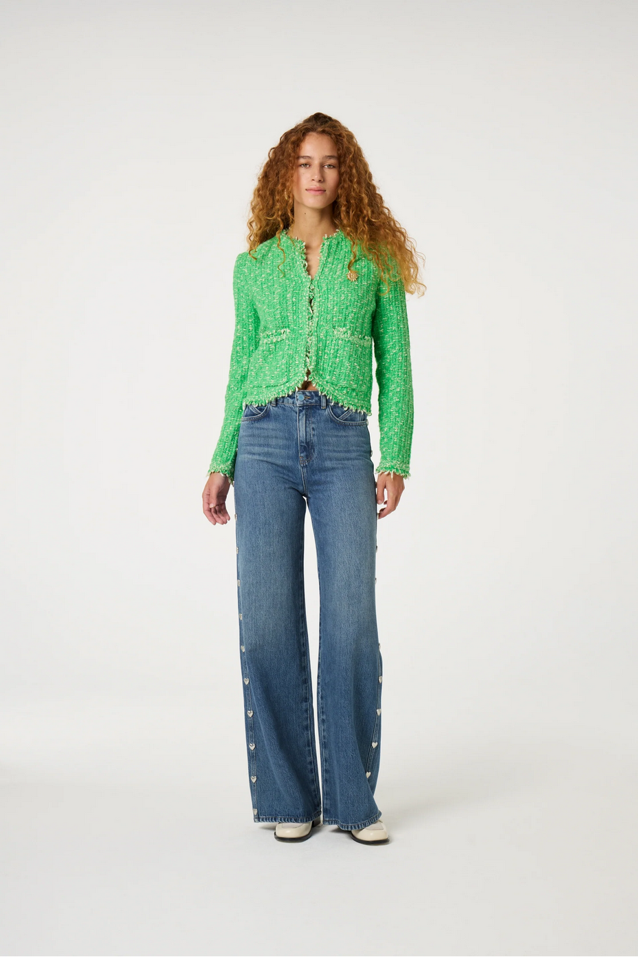 a woman stands and wears a green cardigan and jeans by fabienne chapot on a white background