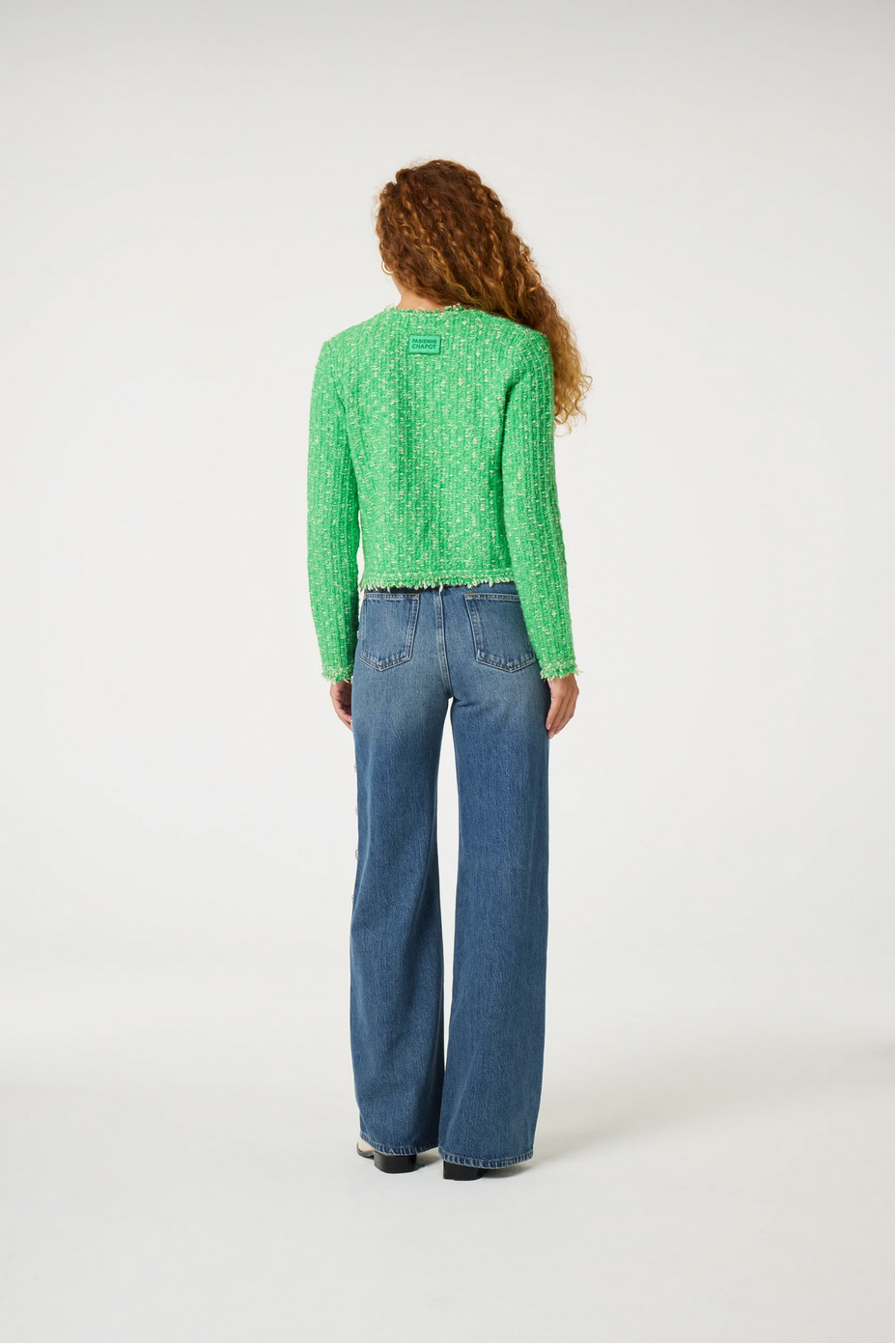 a woman stands and wears a green cardigan and jeans by fabienne chapot on a white background