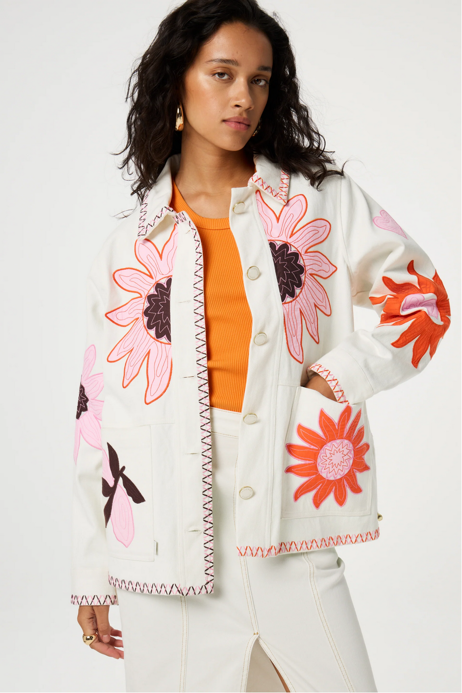 A person wearing the Fabienne Chapot Elody Jacket in Warm White/Floral, paired with an orange top and a white skirt featuring a front slit.