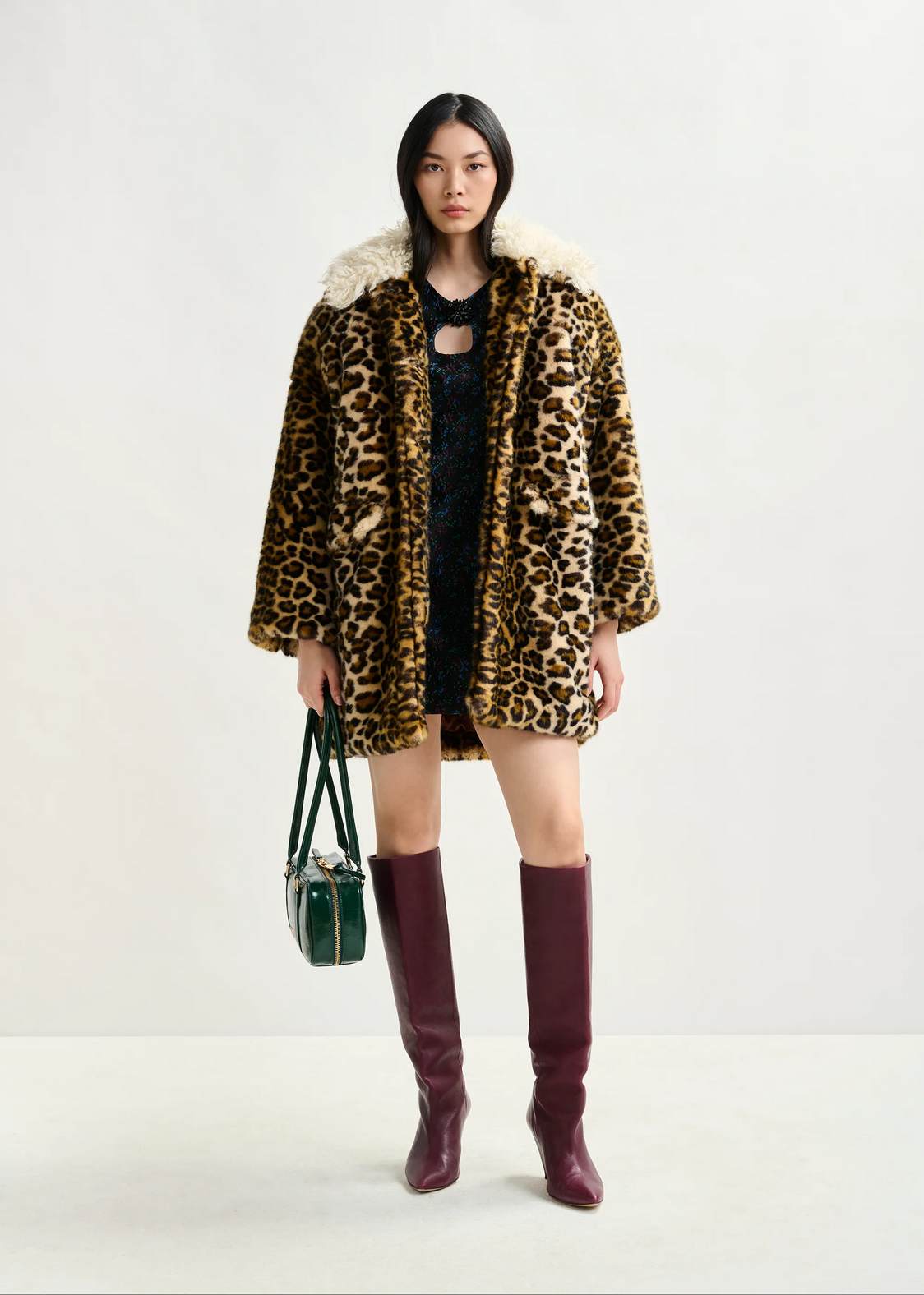 a woman with brown hair wears essentiel antwerp leopard print faux fur coat with cream fluffy collar with red boots against a white background
