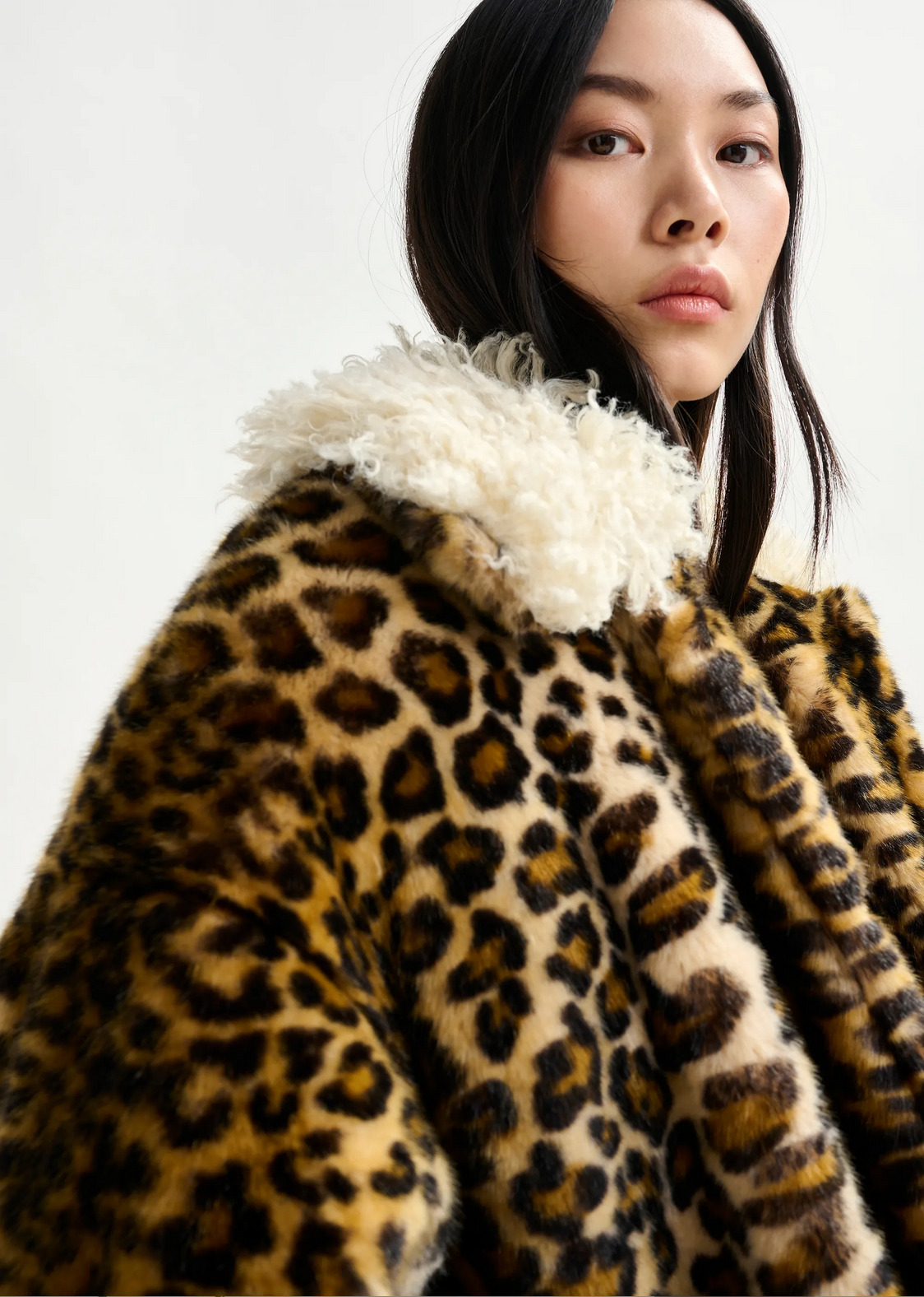 a woman with brown hair wears essentiel antwerp leopard print faux fur coat with cream fluffy collar against a white background