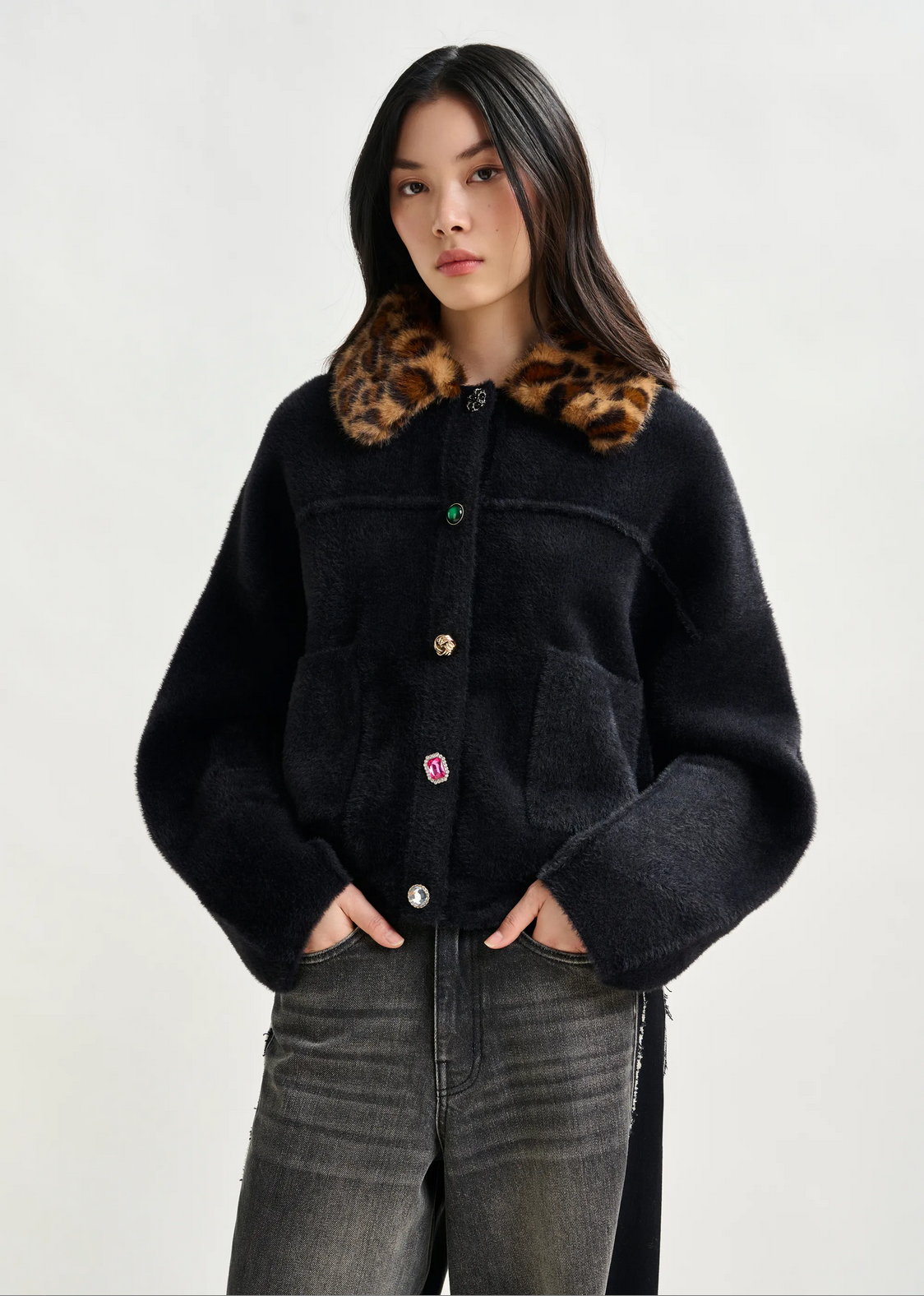 a woman wears an essentiel antwerp black fuzzy knit cardigan with a leopard print collar and grey jeans against a white background
