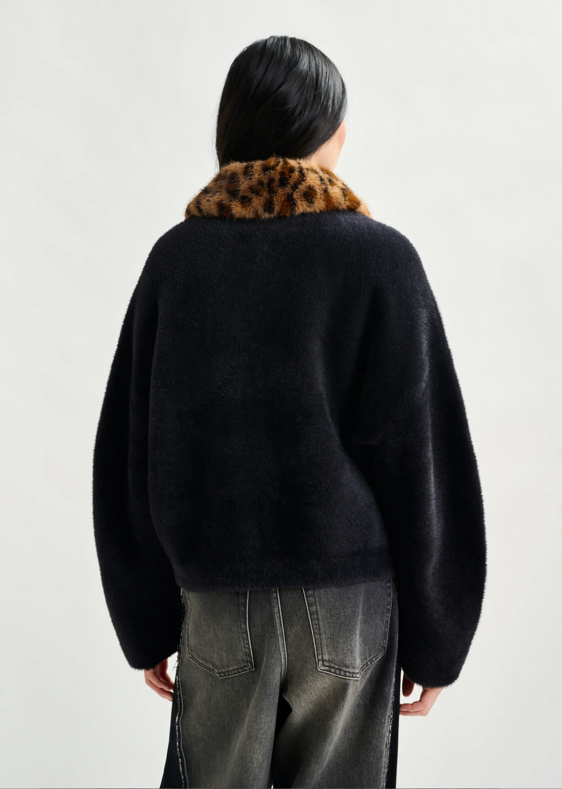 Person wearing a black sweater with a leopard print collar on a white background