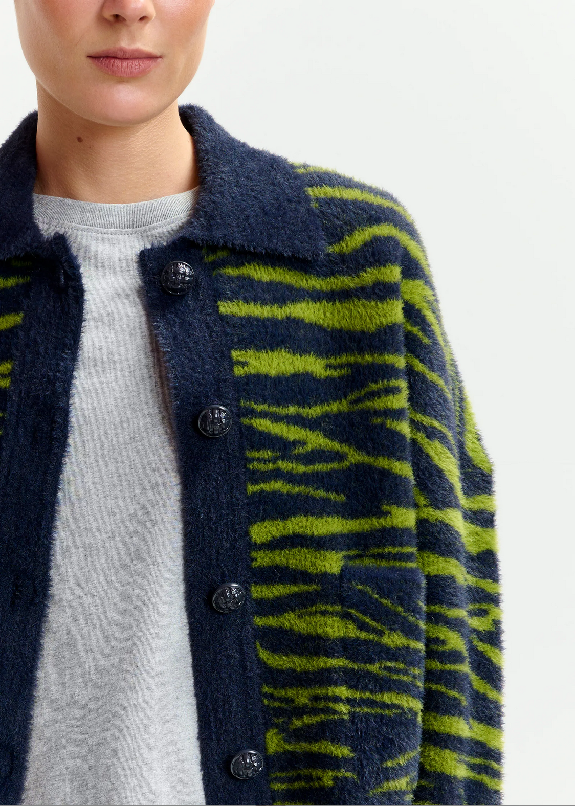 A person wears the Essentiel Antwerp Iger Cardigan in dark green and blue over a light grey top, shown from shoulders to mid-torso against a plain background.