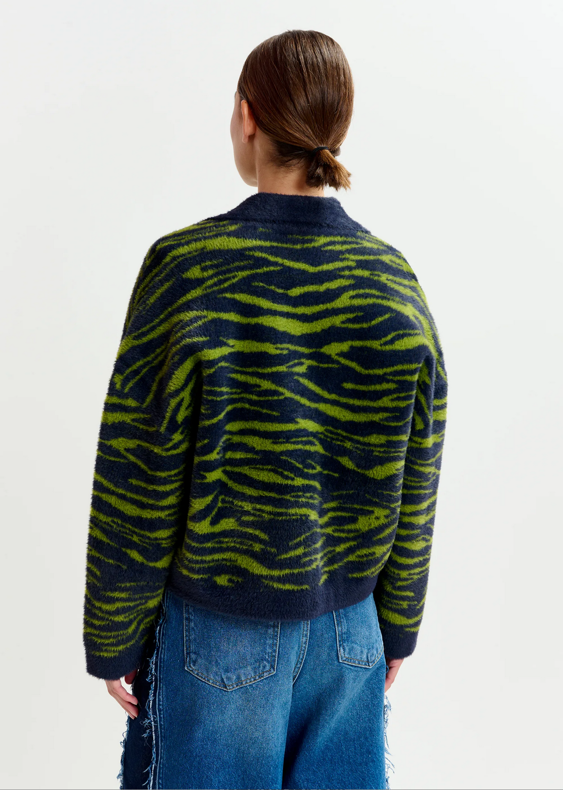 Person faces away, wearing the Essentiel Antwerp Iger Cardigan in dark green and blue with blue denim jeans, set against a plain light background.