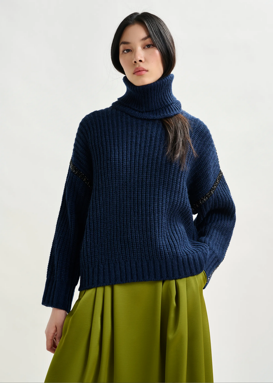 A person wearing the Essentiel Antwerp Indsay Wool Turtleneck in navy and an olive green skirt stands against a plain light background.