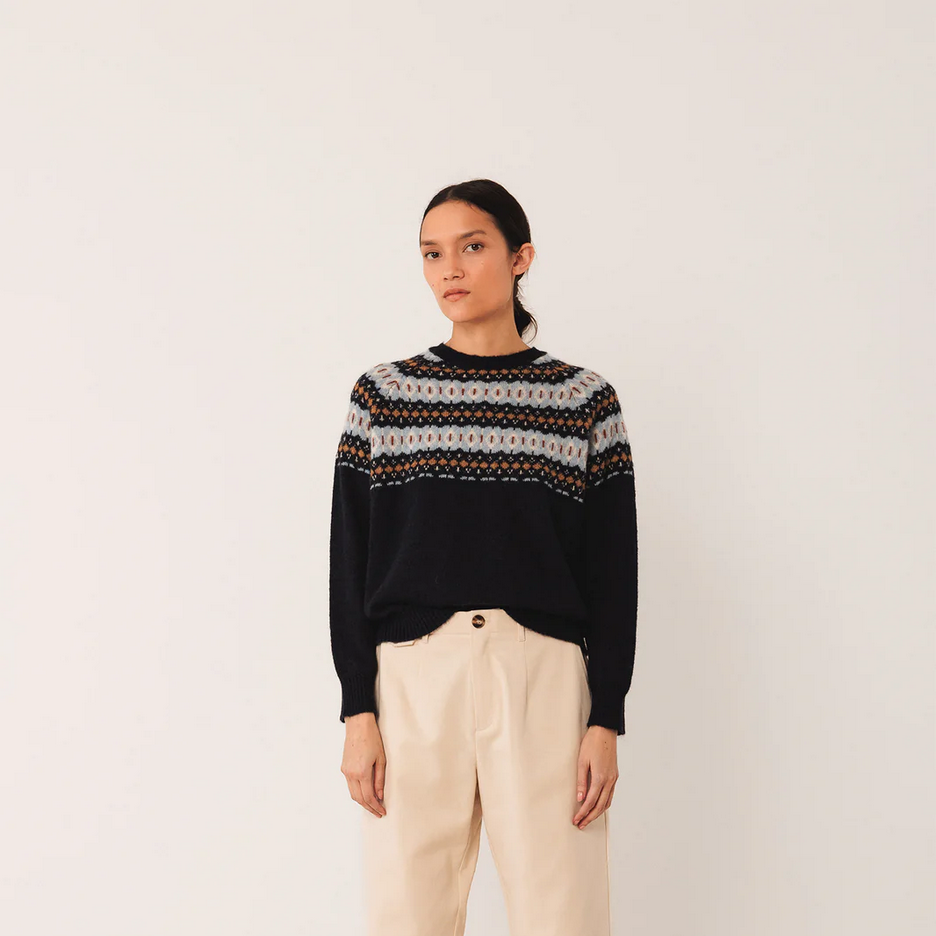 Person wearing a patterned sweater and beige pants on a white background