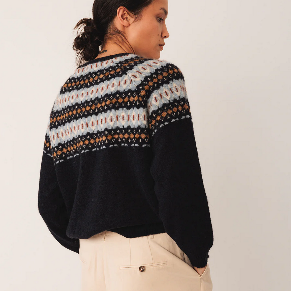 Person wearing a black sweater with a patterned yoke against a plain background