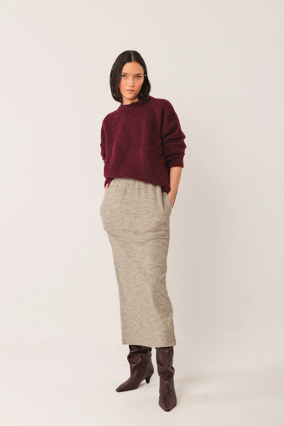 Woman wearing a burgundy sweater and beige skirt on a white background