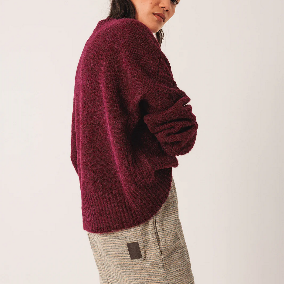 Person wearing a burgundy sweater and beige pants on a white background