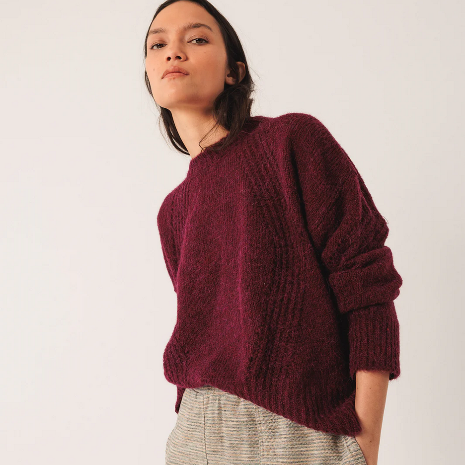 Person wearing a burgundy sweater and light-colored pants against a white background