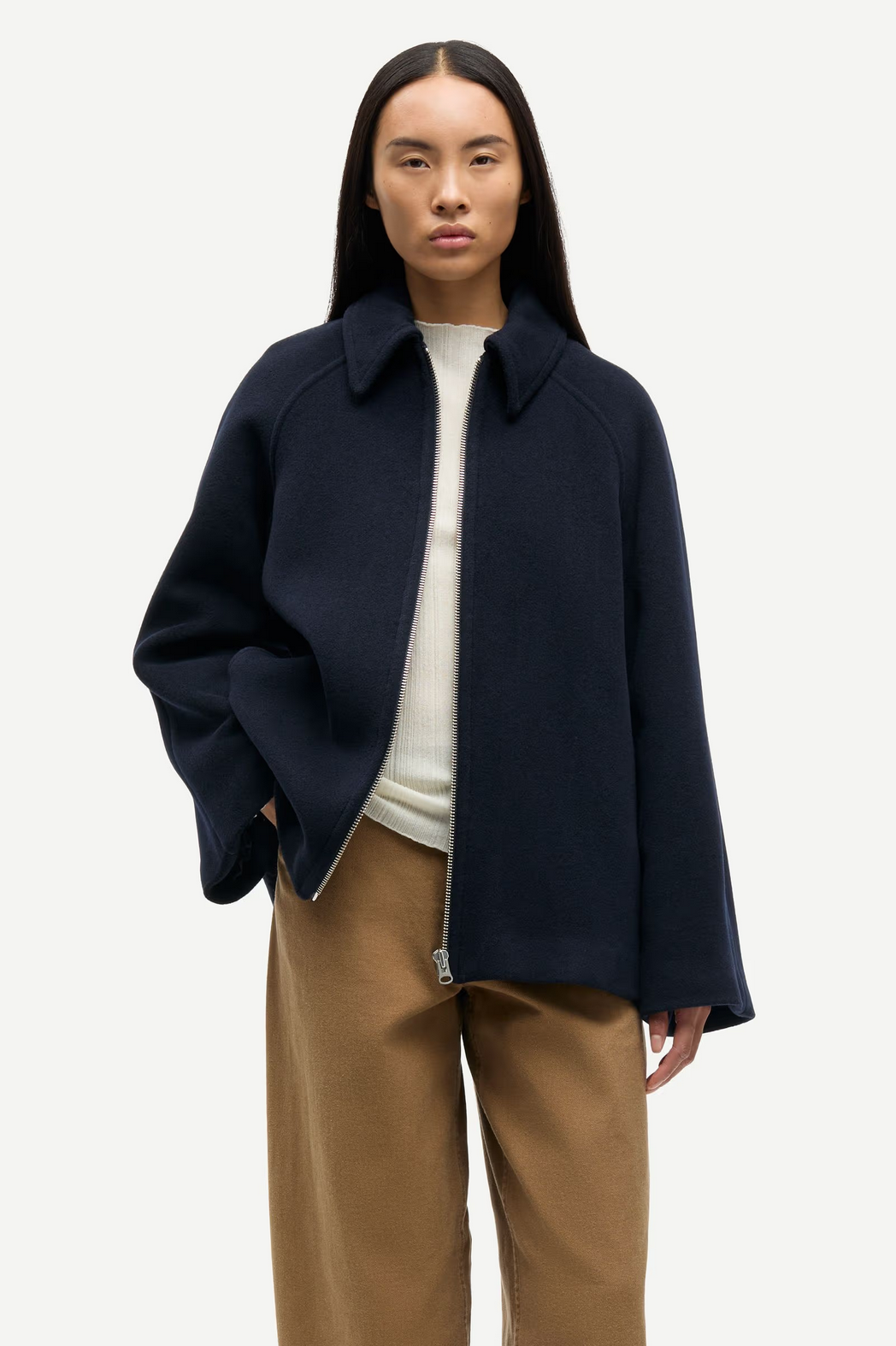 A person wearing the Samsøe Samsøe Alma Jacket - Salute, a navy blue recycled wool coat made in Italy, stands facing forward over a white top and tan pants with one hand in their pocket.
